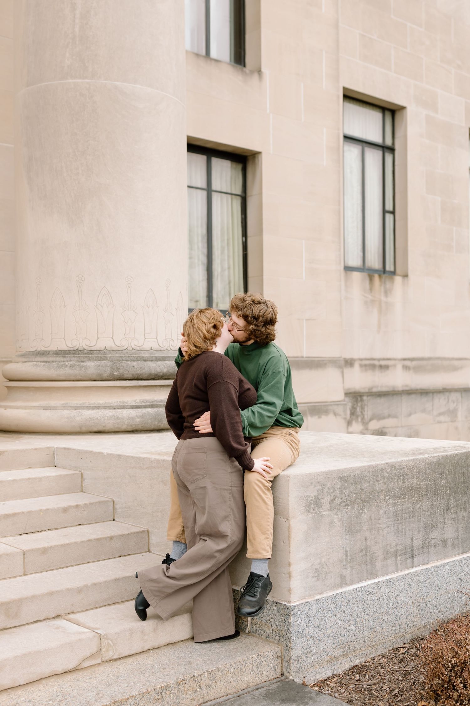 Two people share a romantic moment while sitting on concrete steps outside a building.