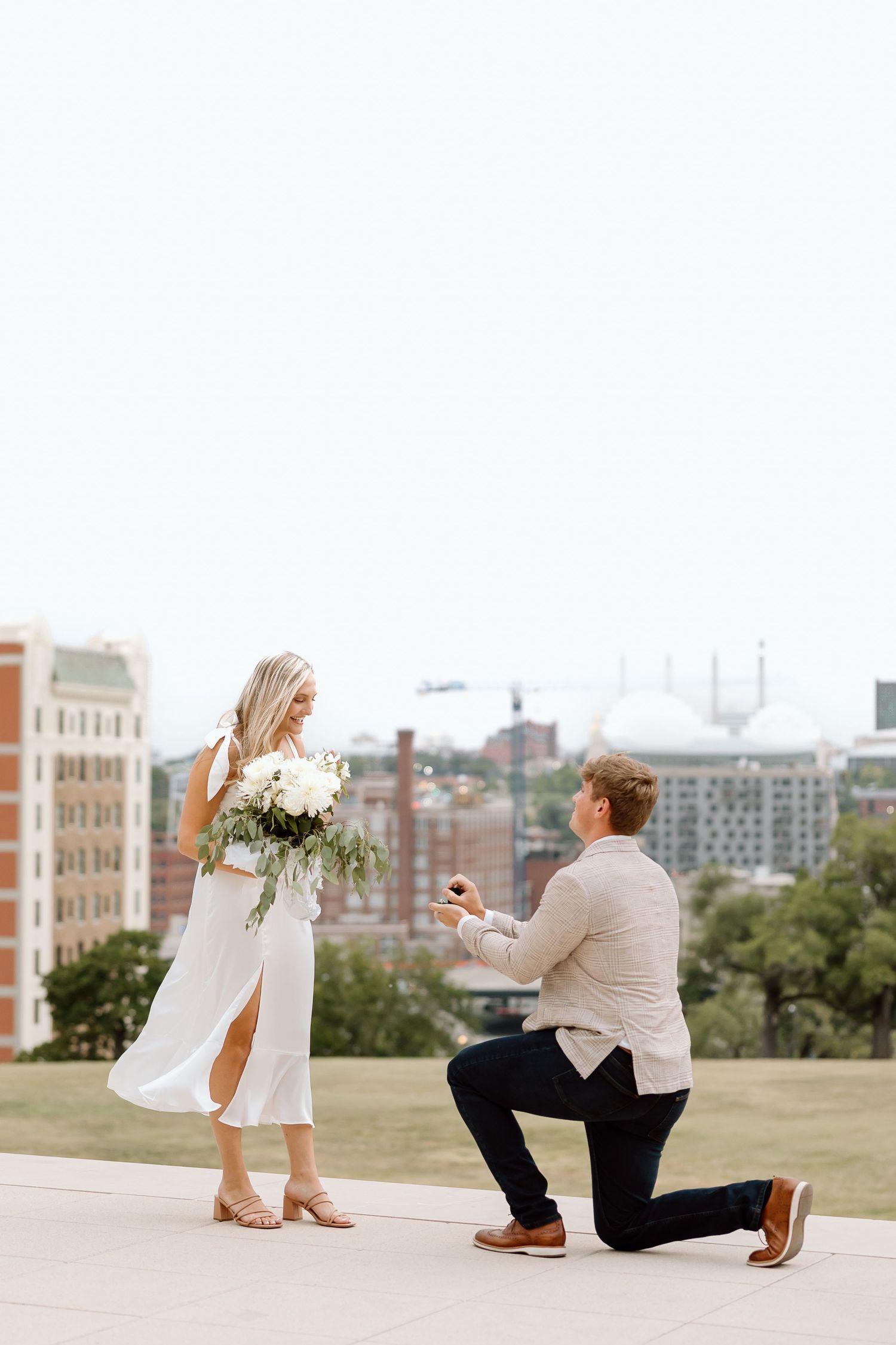 A sequence of photos showing a proposal moment unfolding on a grassy hilltop overlooking a city skyline.