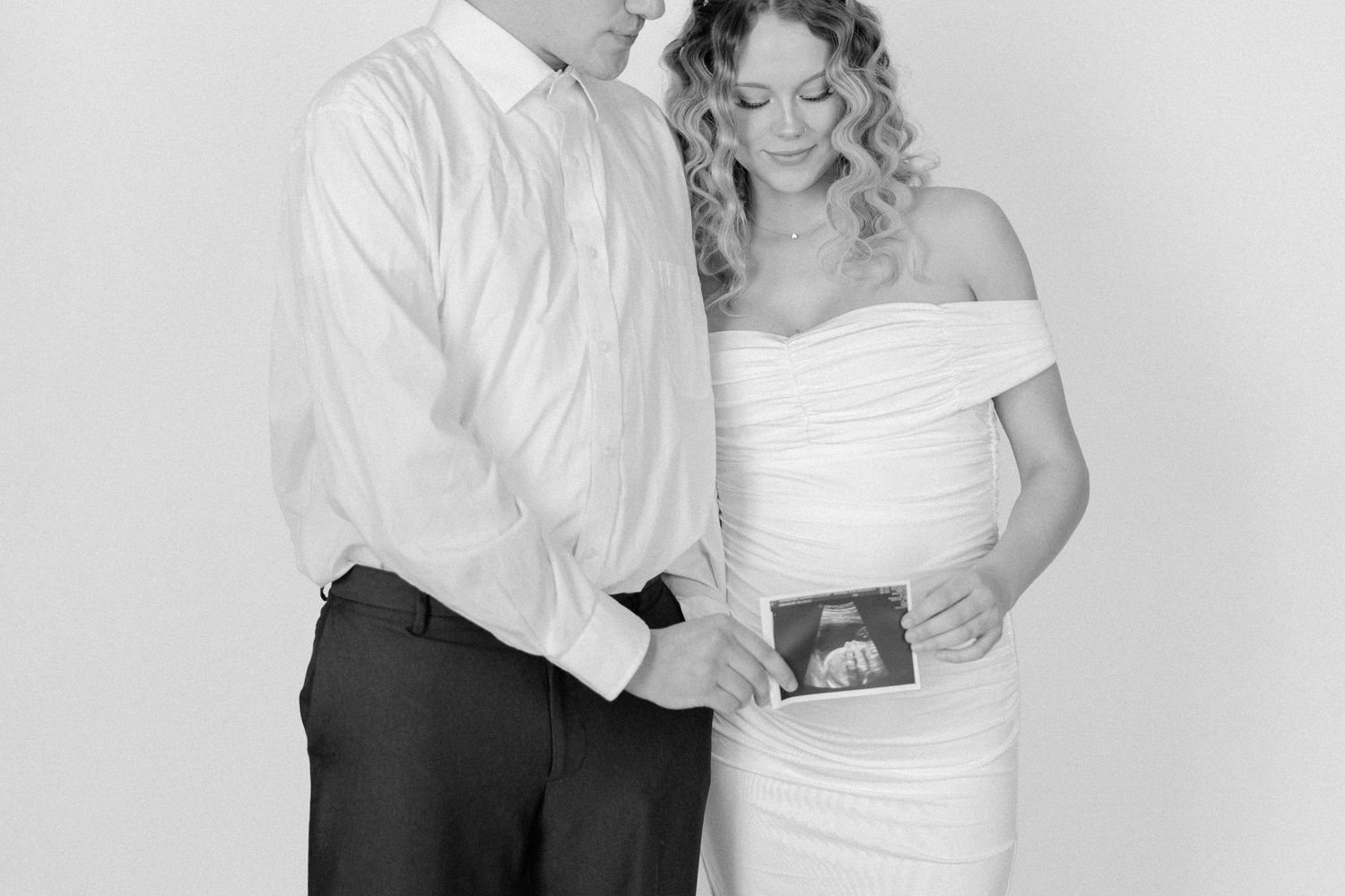 A couple in formal wedding attire dance together in a romantic black and white photograph.