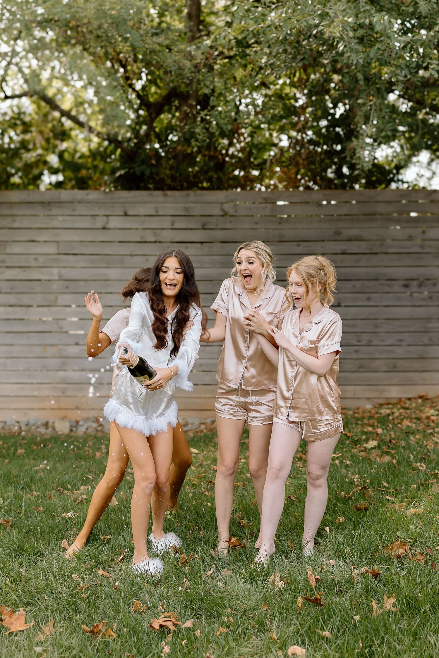 A group of friends in matching outfits dance and laugh together on a grassy lawn during autumn.