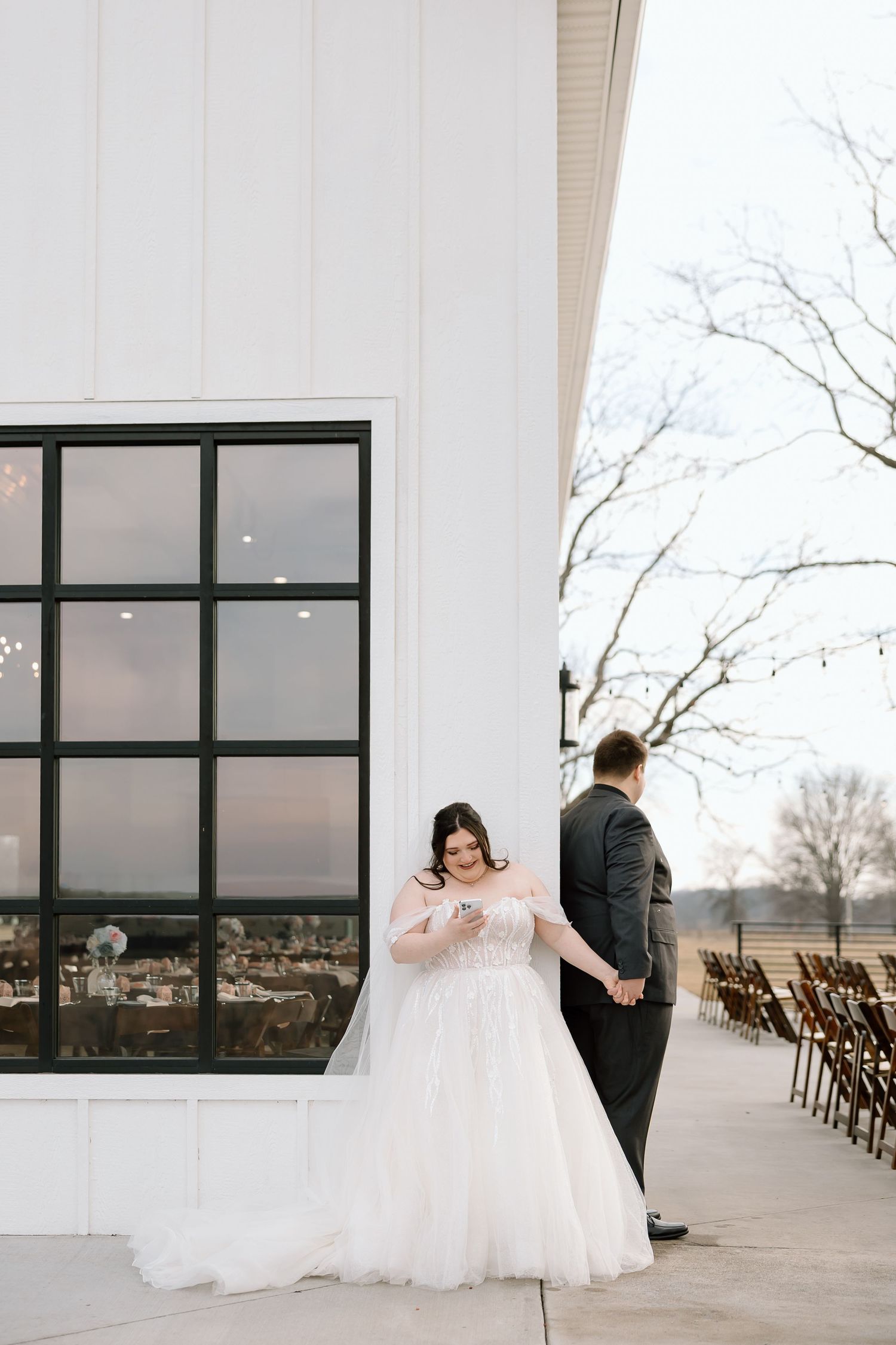 A wedding couple shares intimate moments in a minimalist white venue with large windows overlooking a scenic landscape.