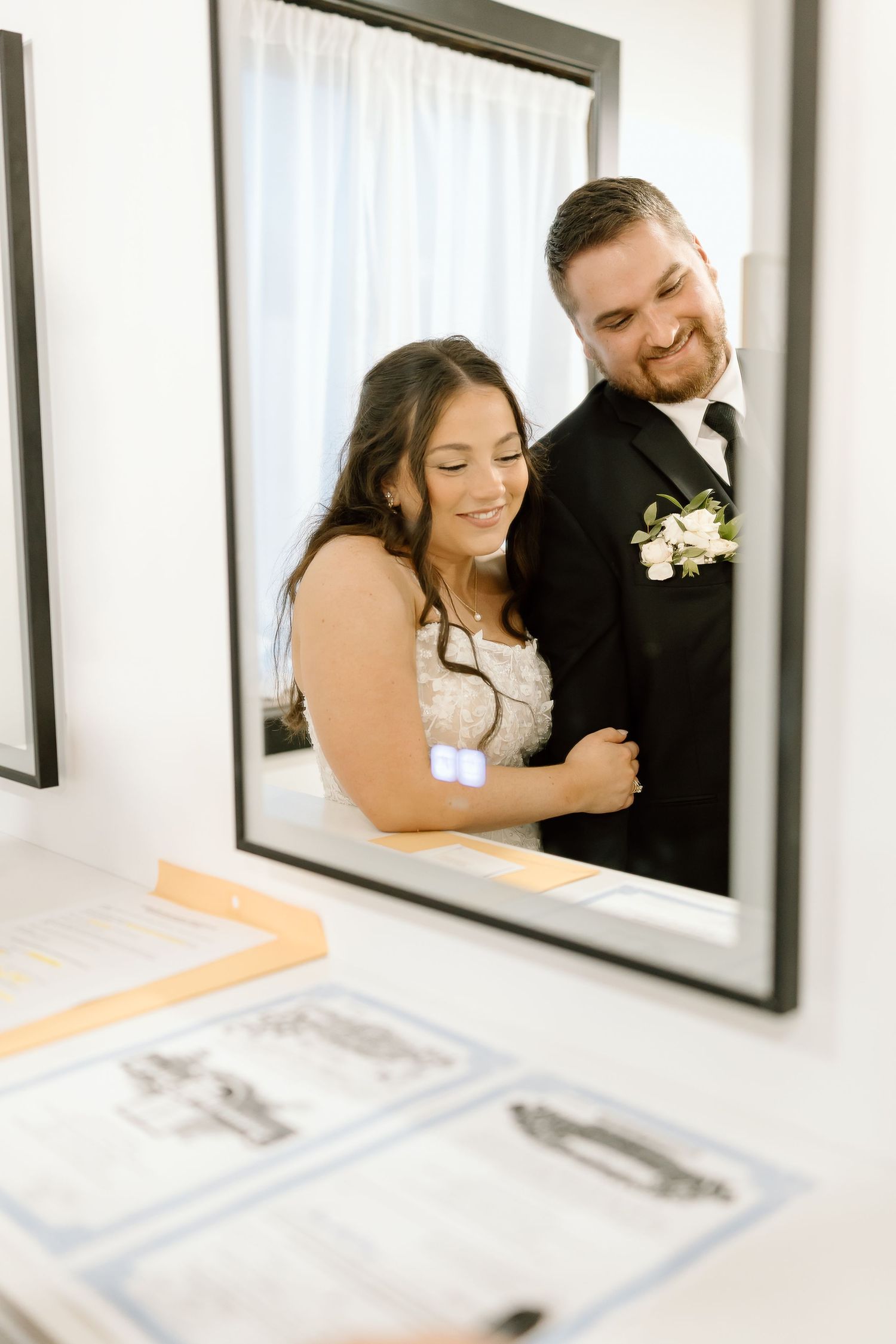 A romantic wedding couple embraces while looking at framed artwork displayed on a white wall.