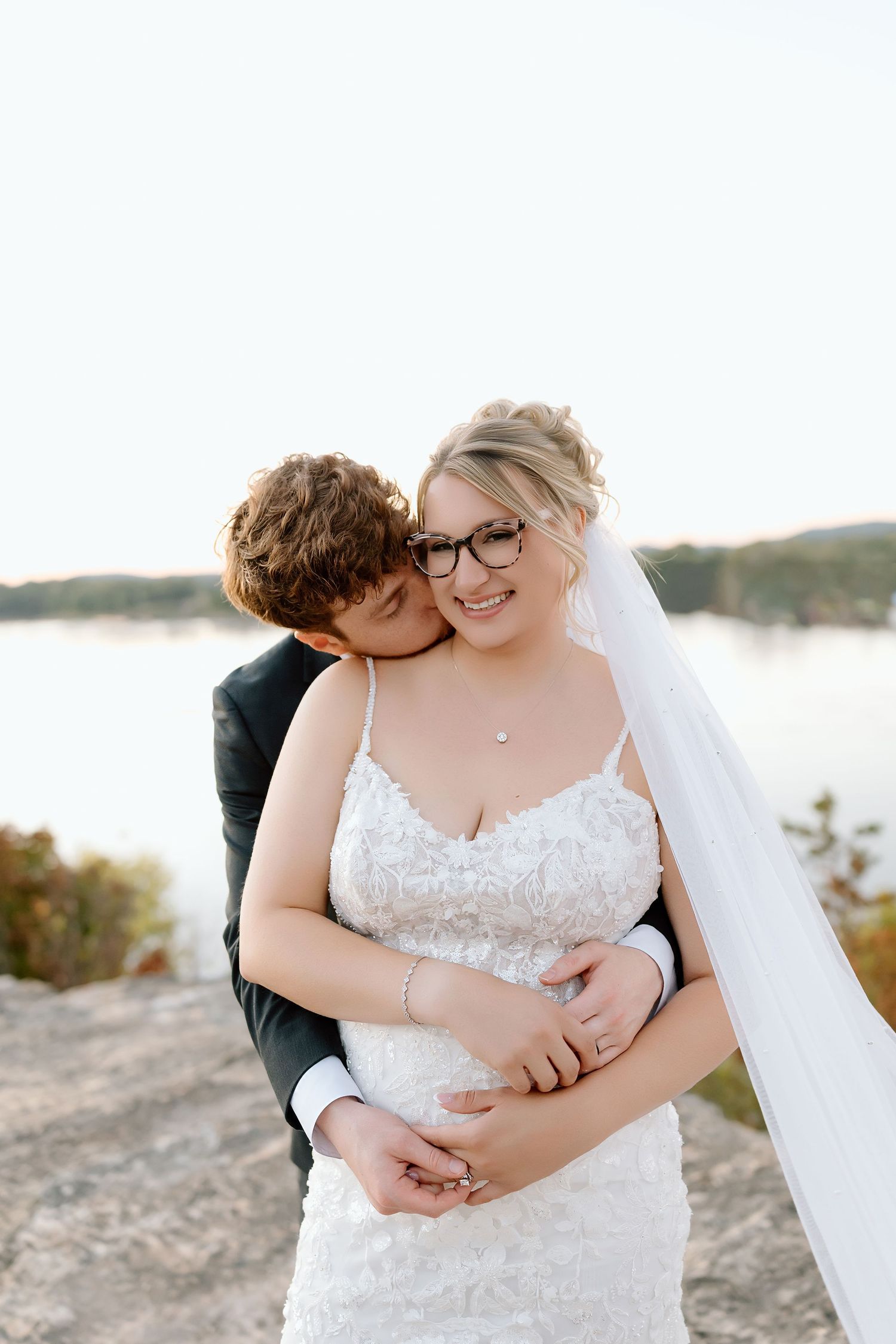 A romantic beach wedding photoshoot shows a couple embracing in white attire against a scenic coastal backdrop.