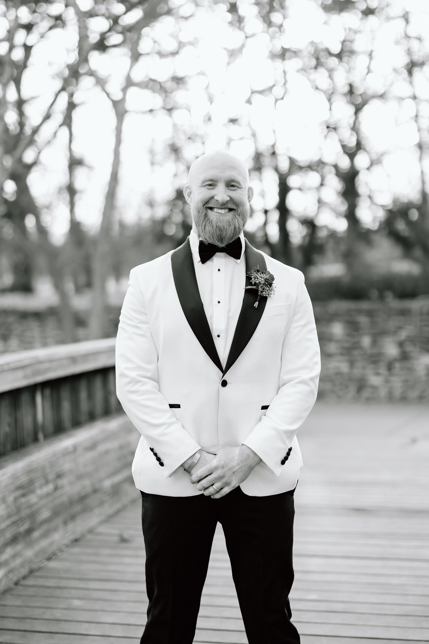 Black and white photo of a person in a white tuxedo jacket and black bow tie standing on a wooden boardwalk.