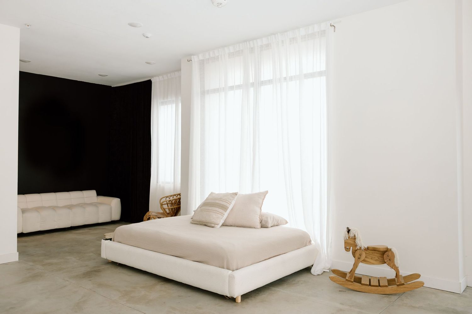 Modern minimalist white bedroom interior with sheer curtains and rocking horse decor creates a serene atmosphere.