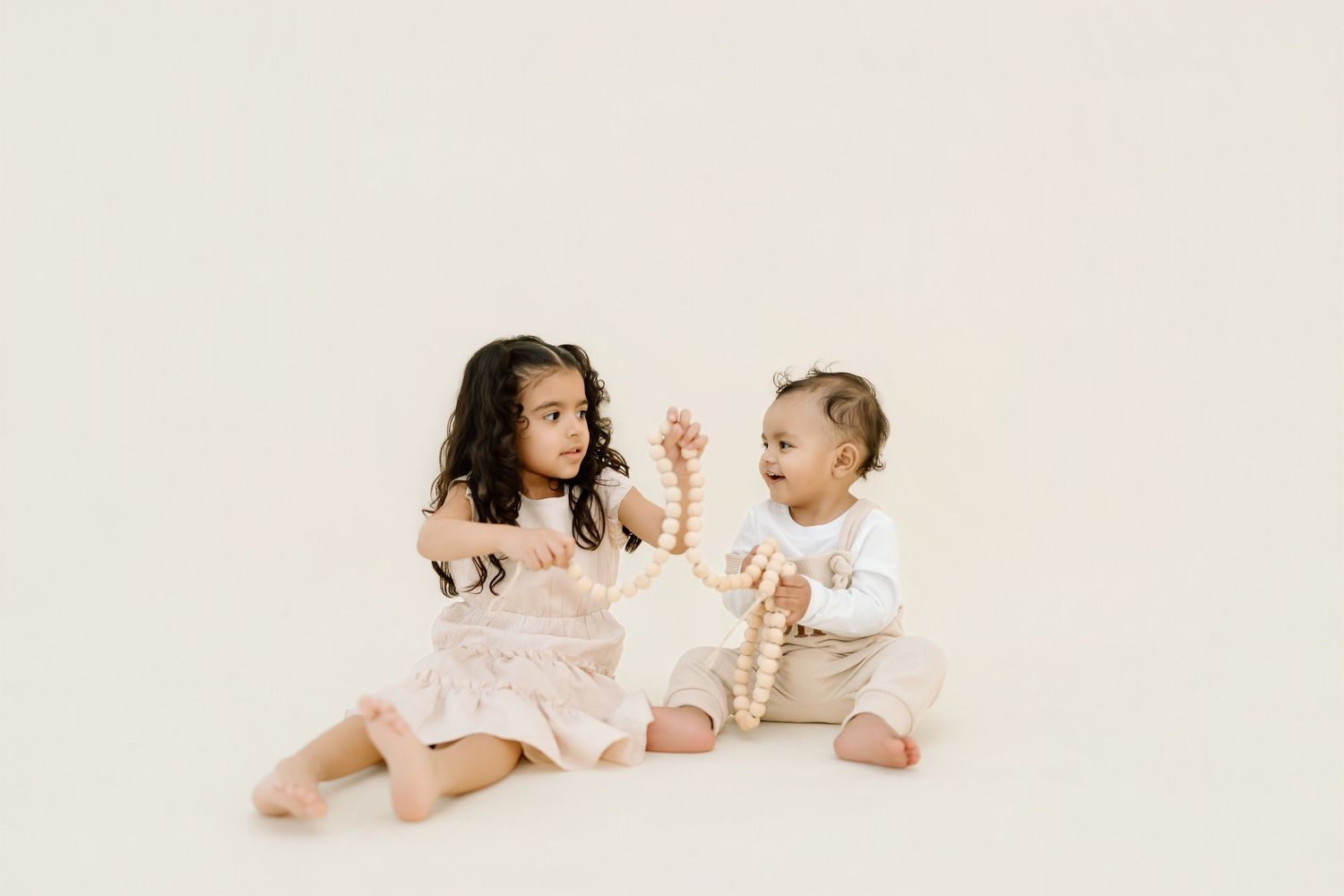 Two siblings laying on a white blanket in matching outfits share sweet moments together during a photo session.