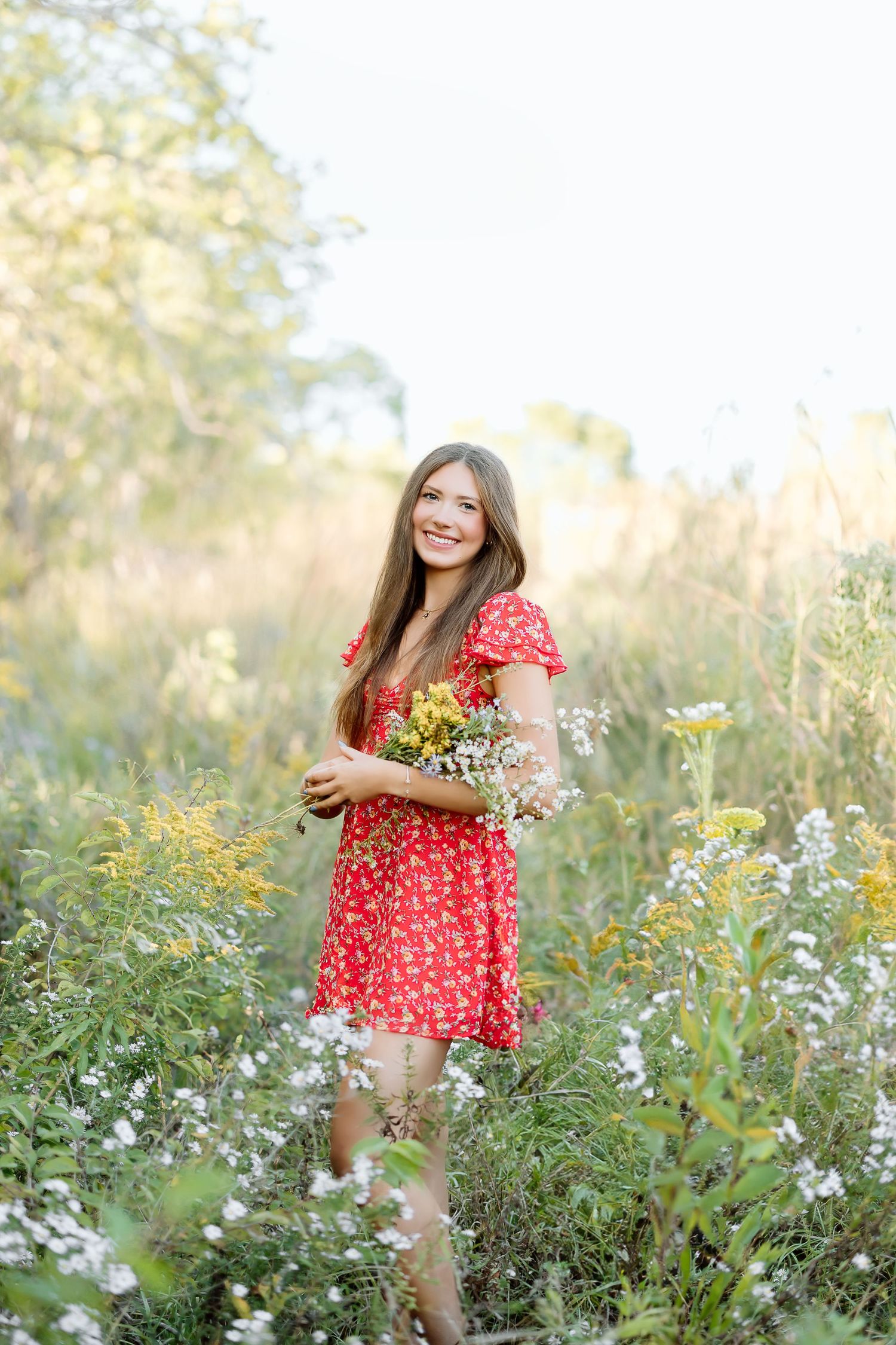A person in a red floral dress stands among blooming wildflowers in a sunny meadow during golden hour.