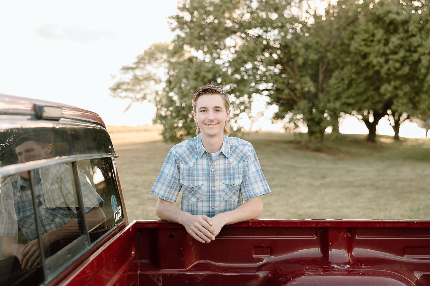 Someone stands in the back of a red pickup truck at sunset with trees in the background.
