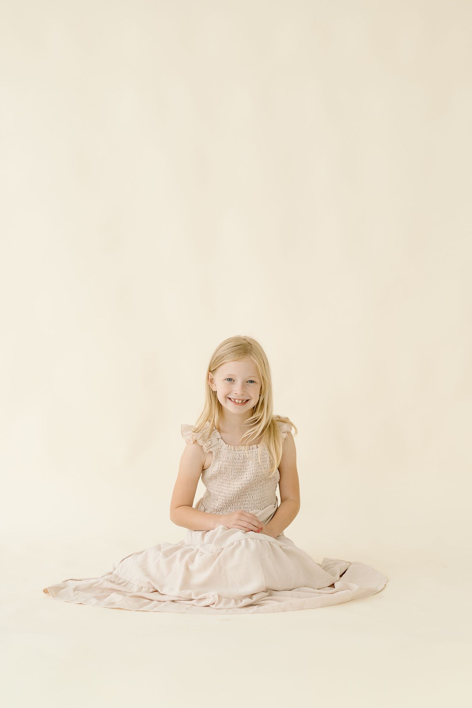 A joyful child wearing a white dress sits on a cream colored background in a series of connected photos.
