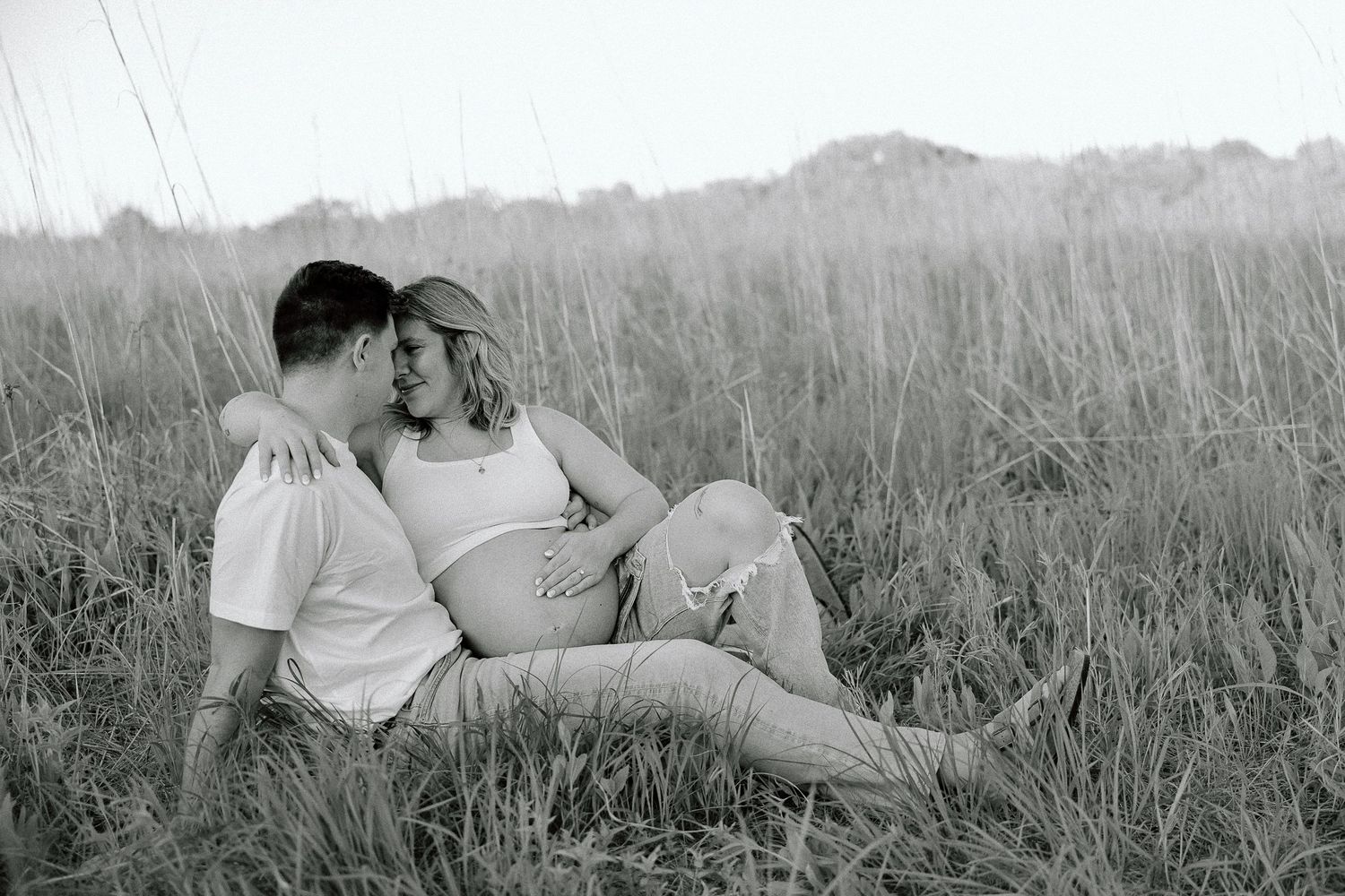 Black and white photo series of a couple embracing in tall grass at sunset.