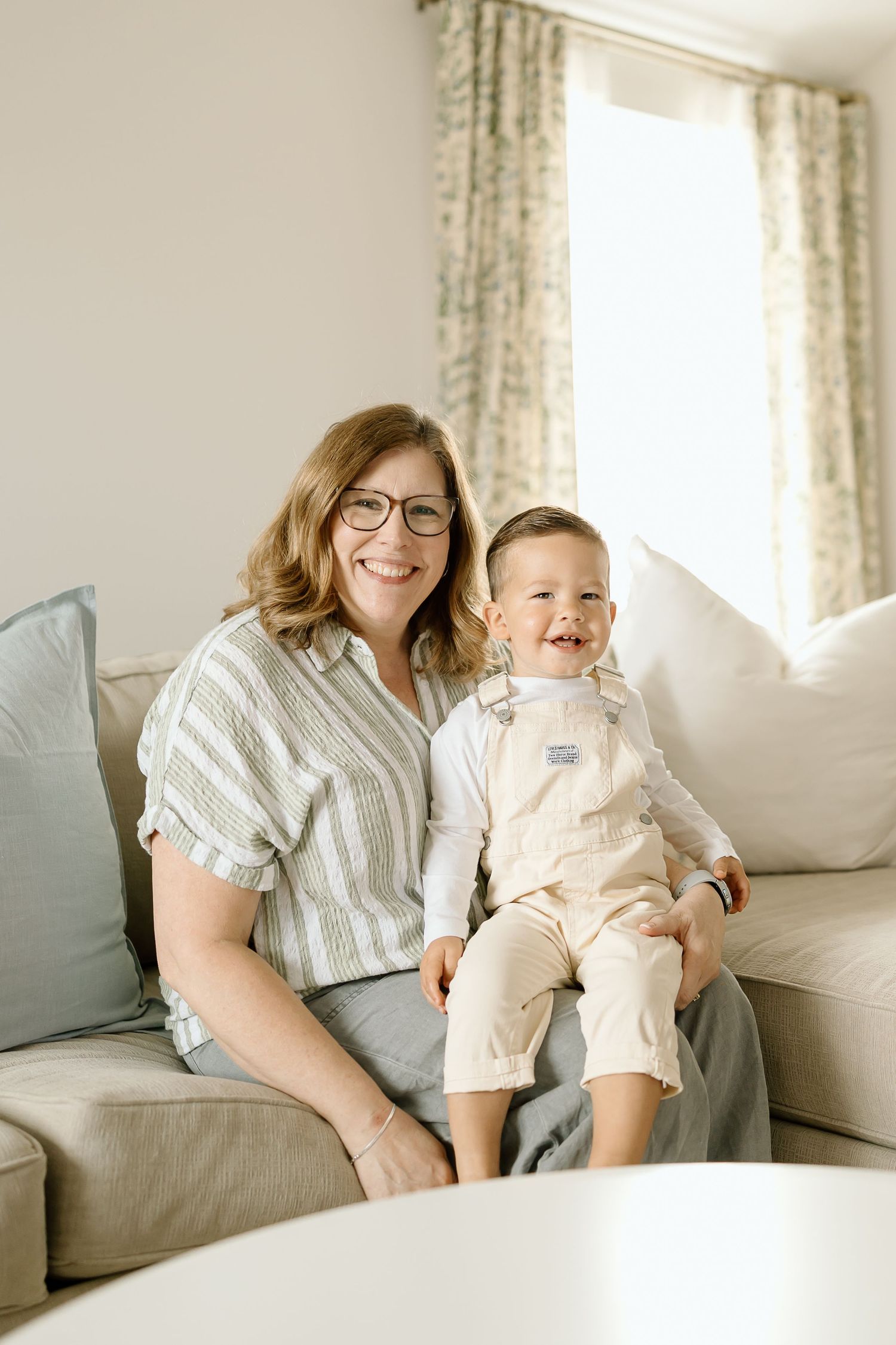 A joyful moment shared between a parent and child laughing together on a light gray couch in a bright room.