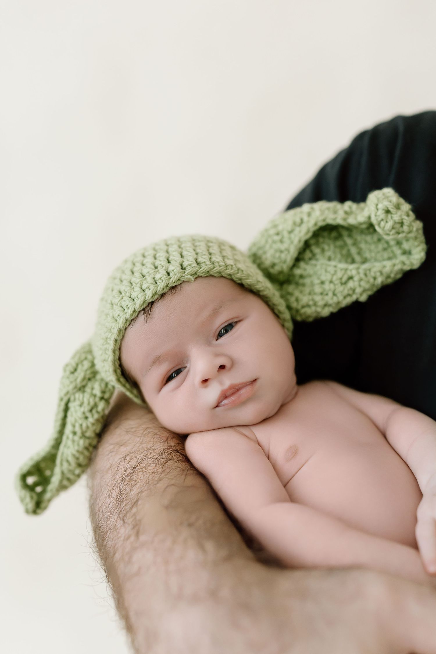 A sleeping newborn baby wearing a light green knitted hat lies on a soft blanket.