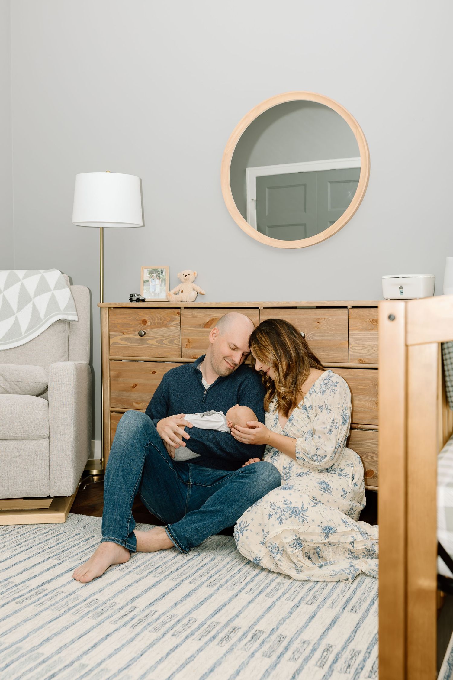 Couple sitting together on a gray and white striped mattress in front of wooden furniture in a minimalist bedroom.