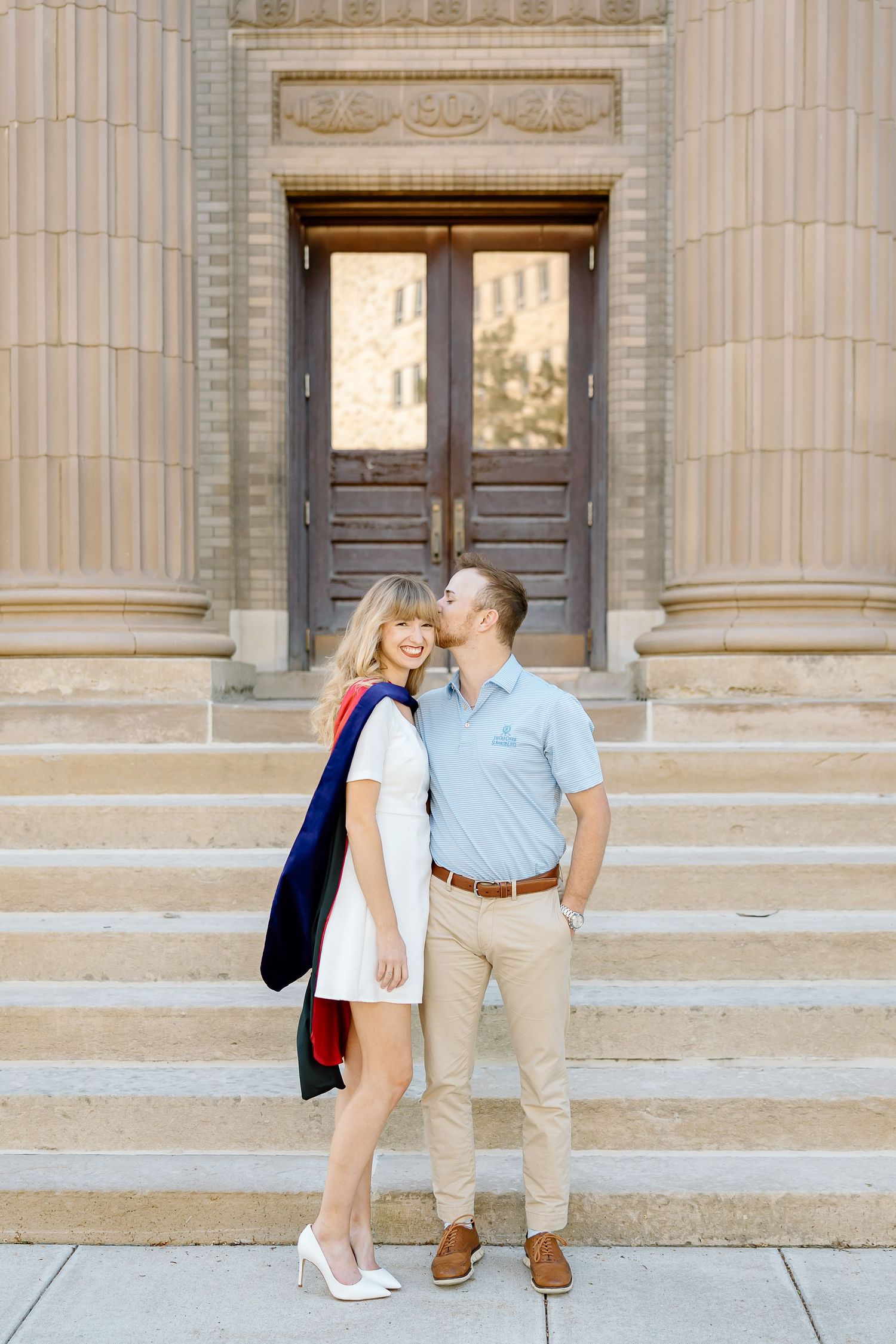 A couple shares a romantic moment on the steps of a grand building with classical columns.