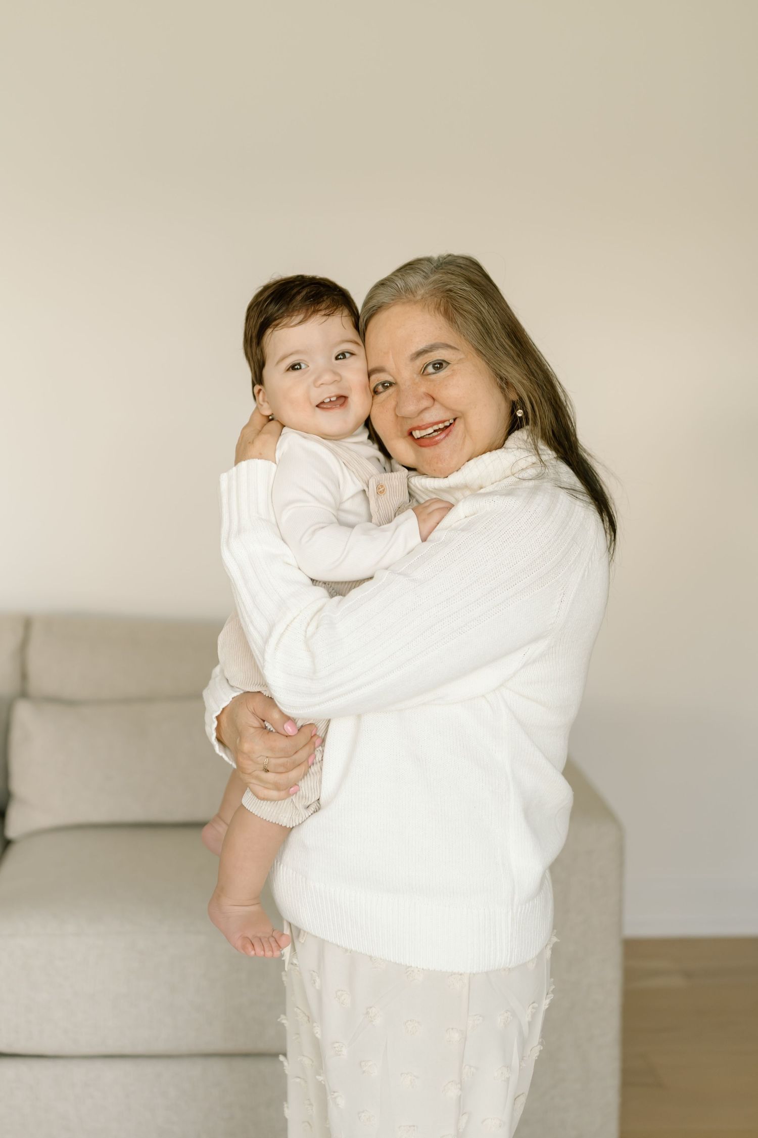A parent and child dressed in all white embrace and smile together in a bright minimalist setting.