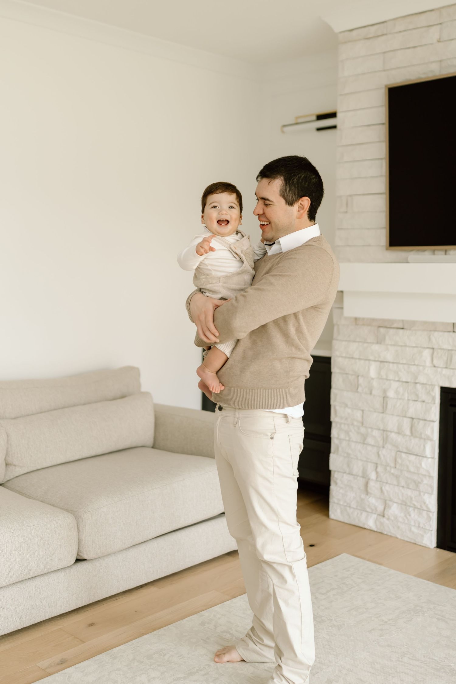 Parent and baby in white outfits playing together in a minimalist white living room with hardwood floors.
