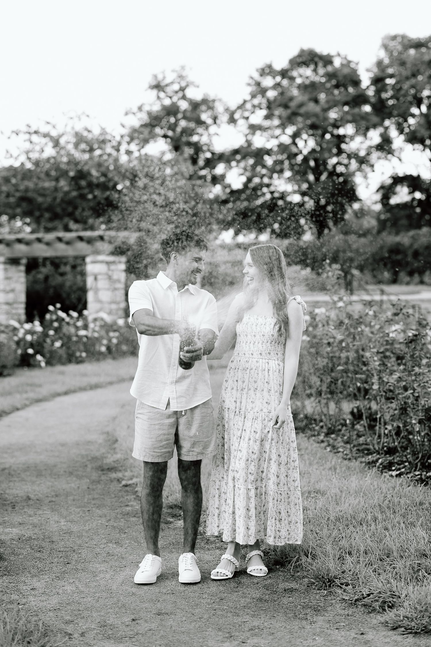 Black and white photo series of two small children in white outfits walking together in a garden path.