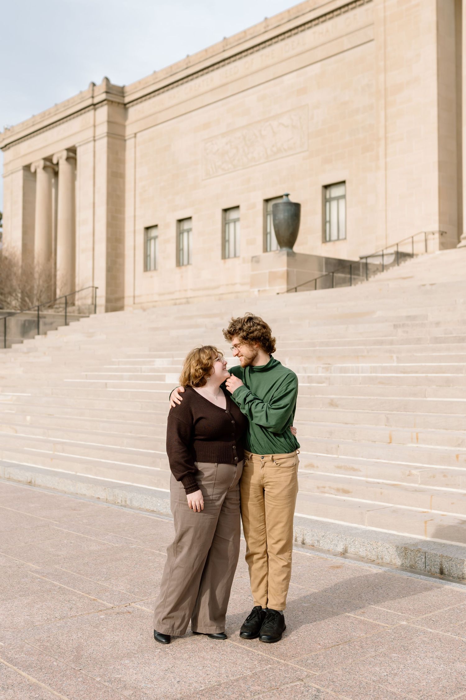 A couple shares an intimate moment on stone steps outside a modern building in a romantic photoshoot series.