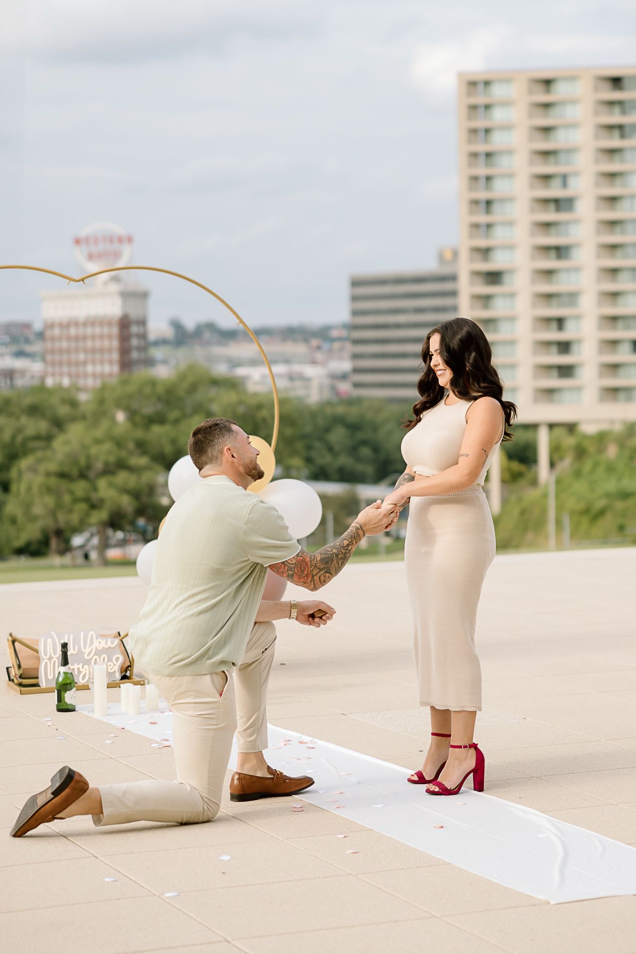 Couple in matching outfits posing playfully with balloons on an urban rooftop terrace.