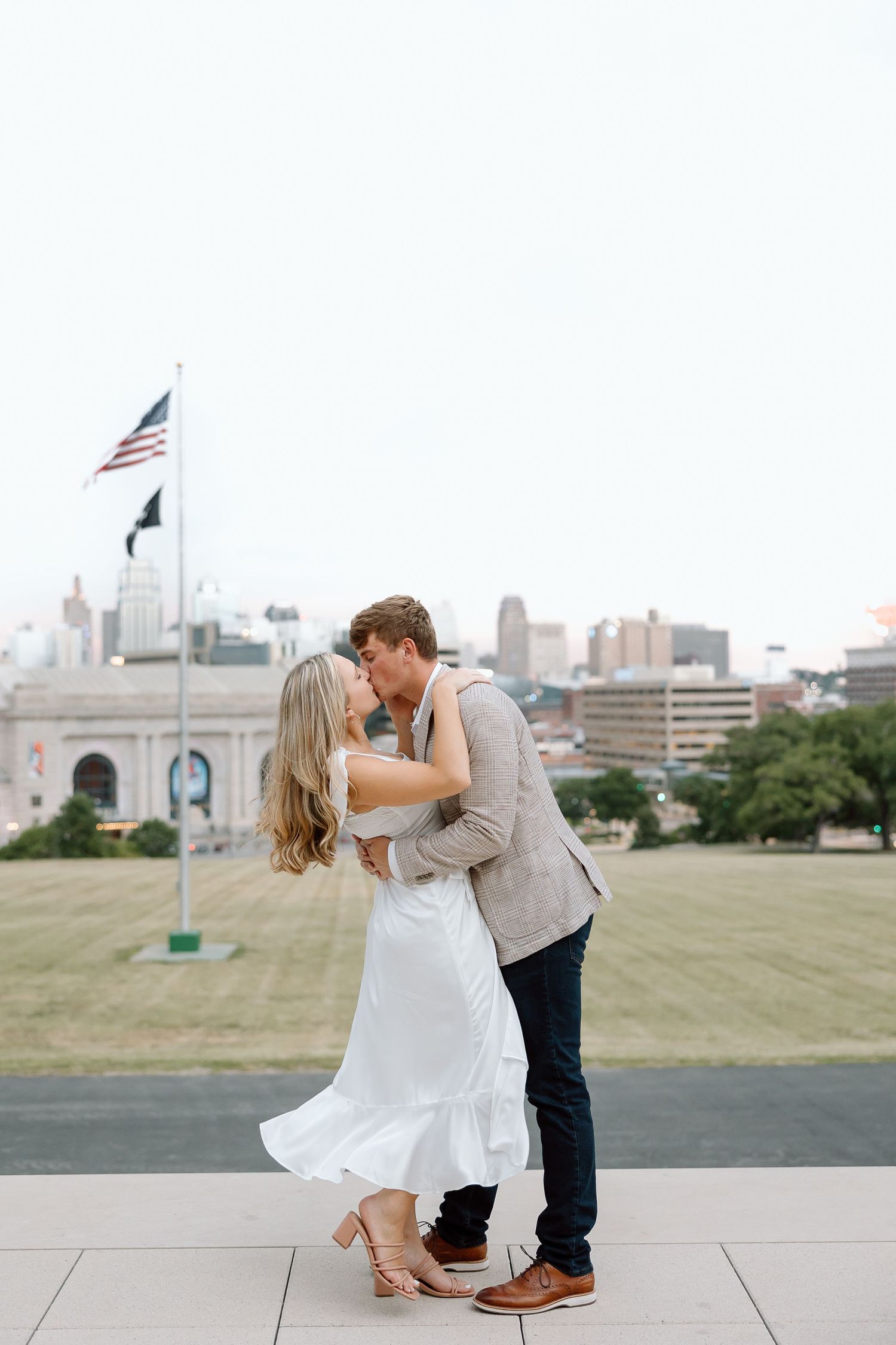 A couple shares a romantic kiss in a series of engagement photos with a city skyline and American flag in the background.