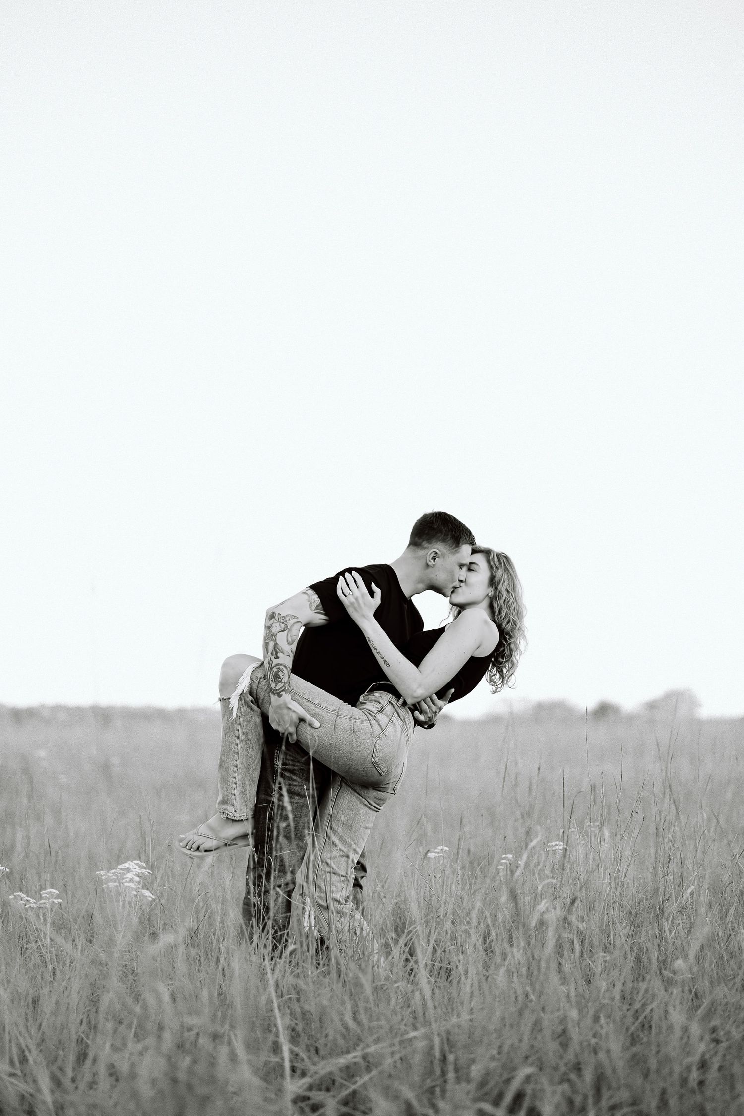 A romantic black and white photo series showing a couple embracing and kissing in a serene meadow field.