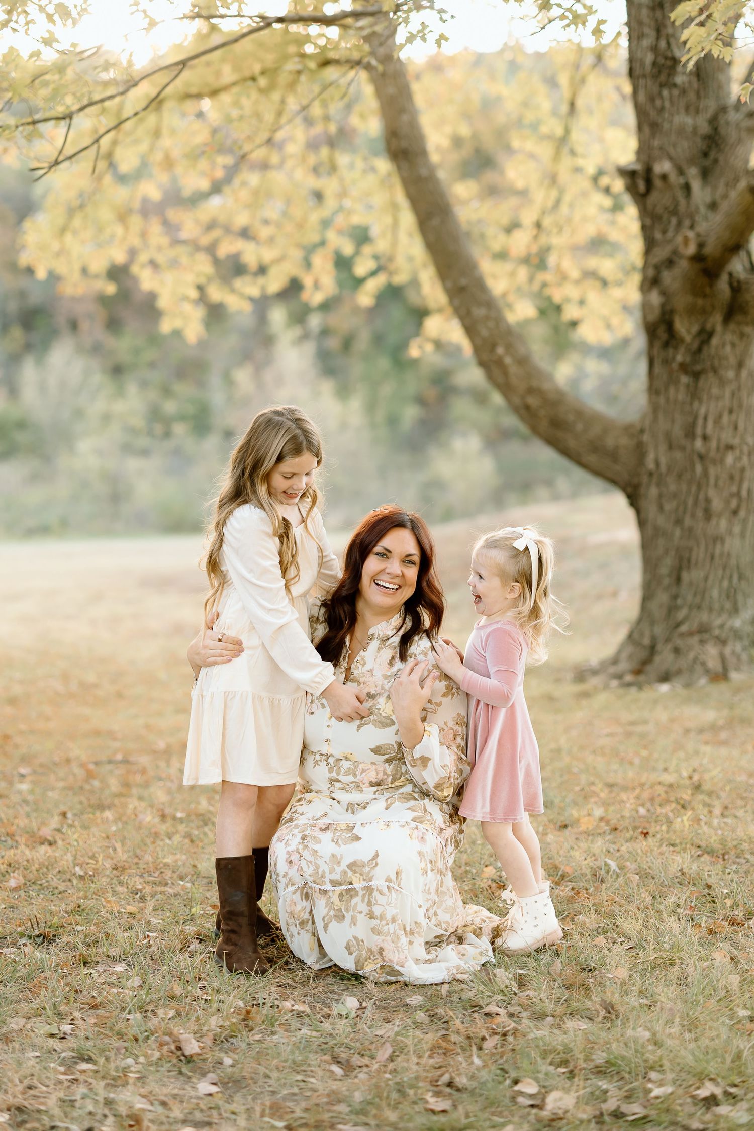 A family shares a tender moment together under a large tree during golden hour in an autumn field.