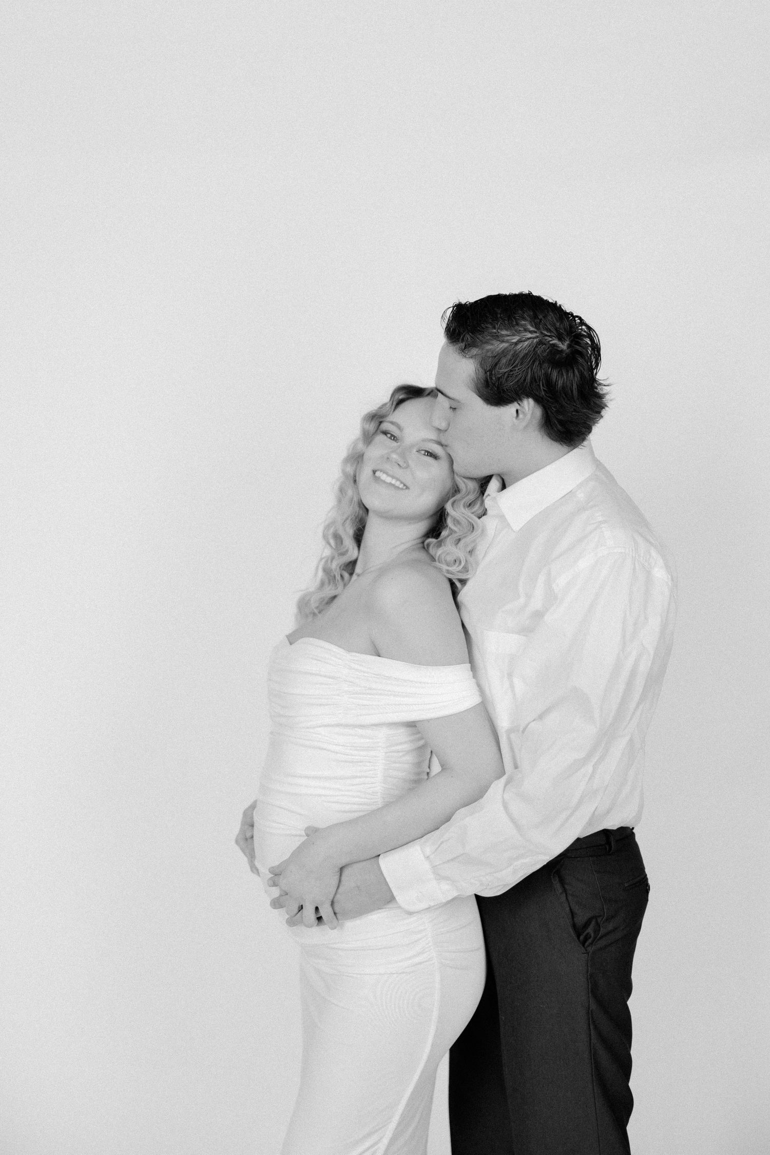 A couple in formal attire embraces in a romantic pose against a light gray background in a series of photos.