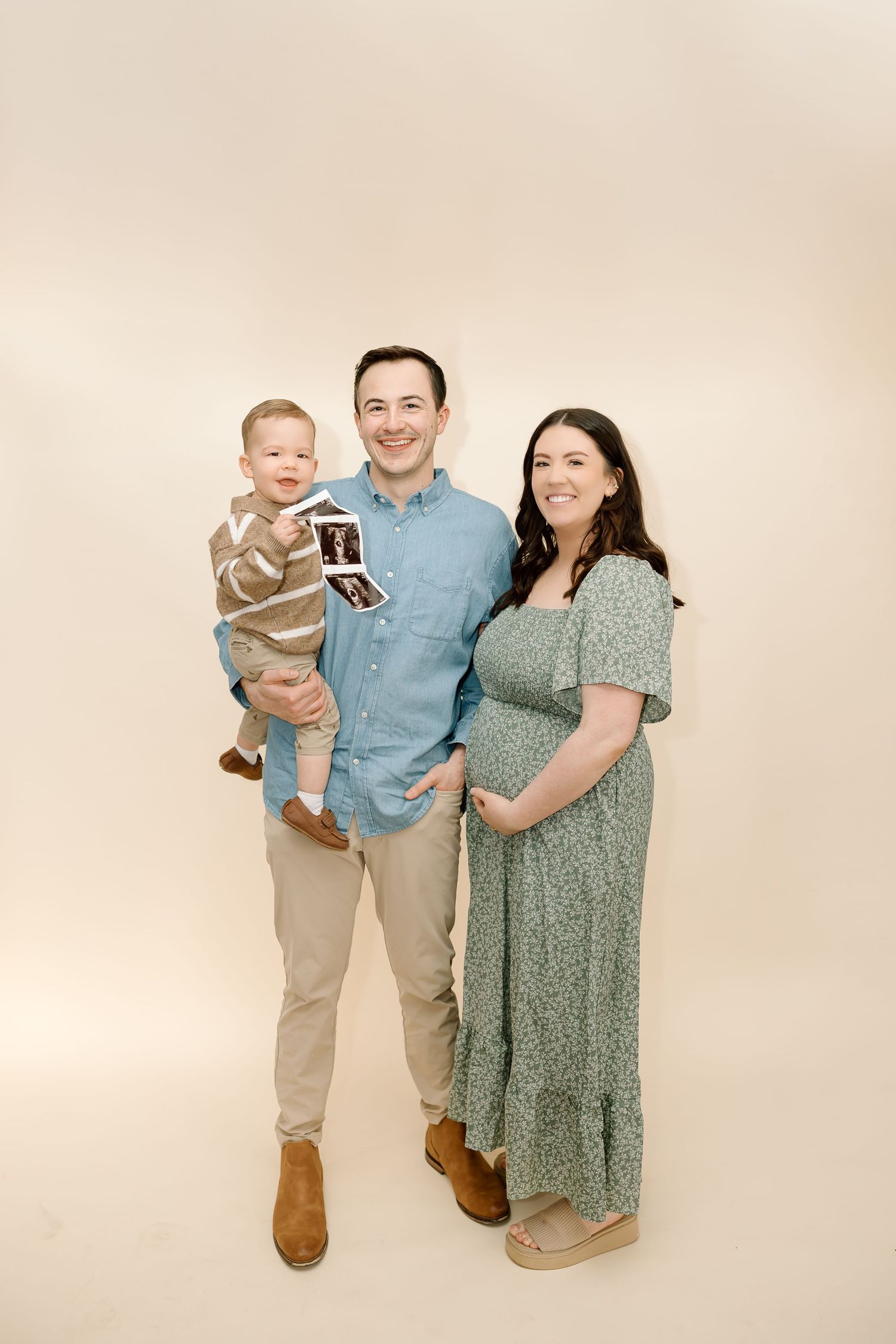Family wearing coordinating outfits in soft blue and sage green poses together against cream background for portrait.
