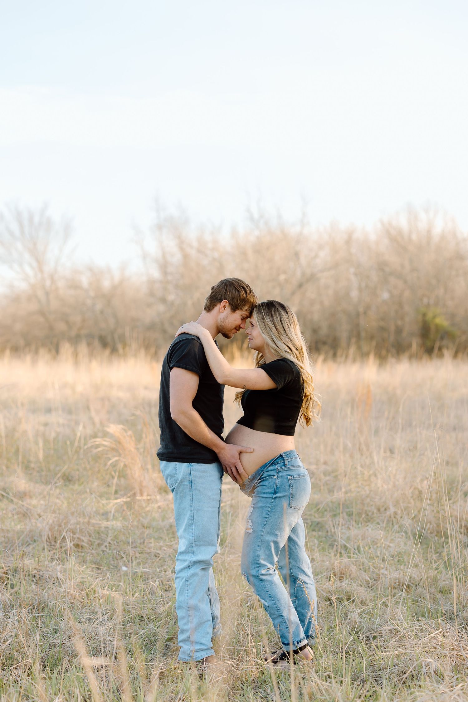 A romantic couple embraces in a sun-lit field of tall grass during golden hour.