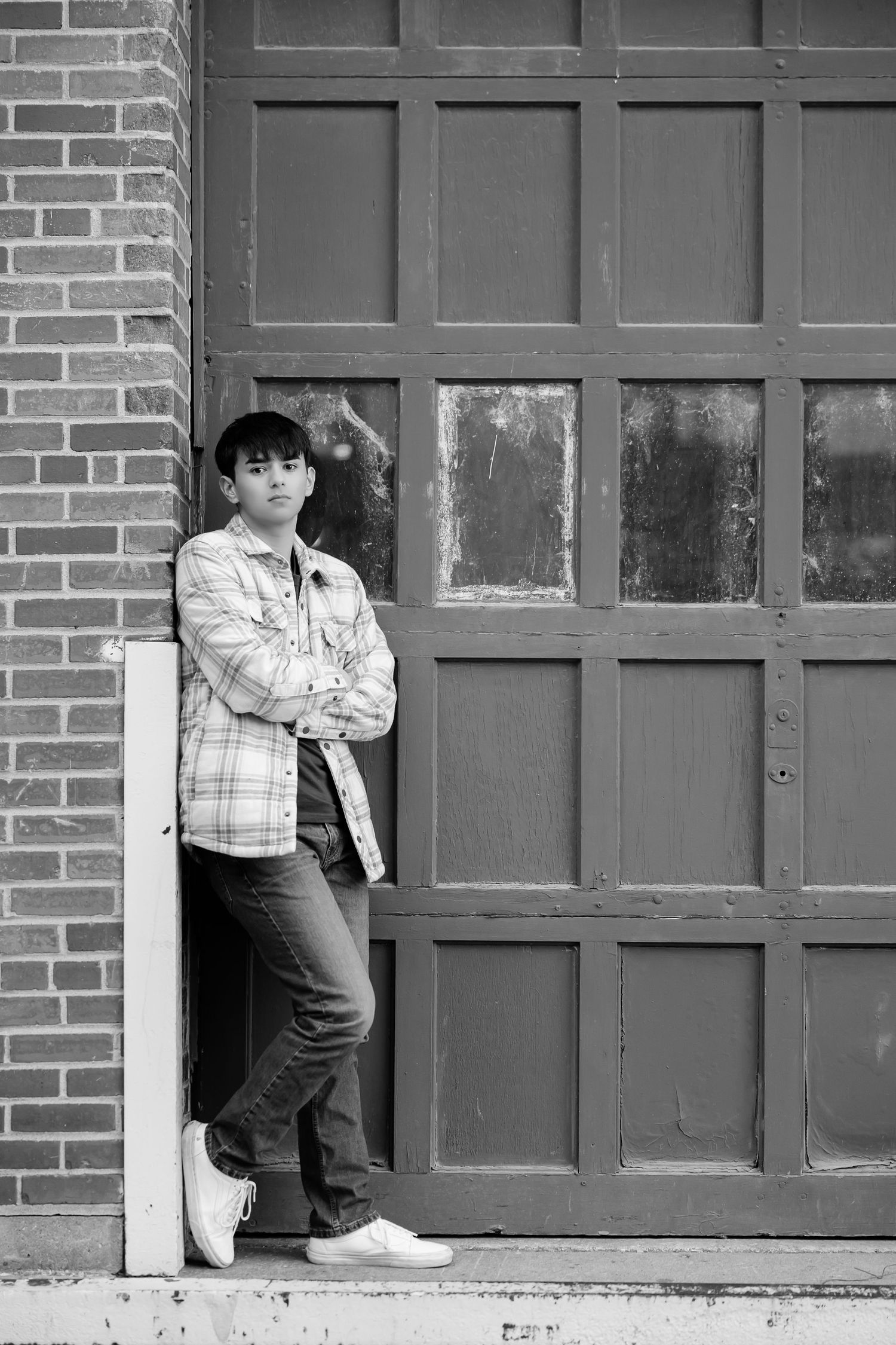 Black and white portrait of person in casual attire standing against industrial door.