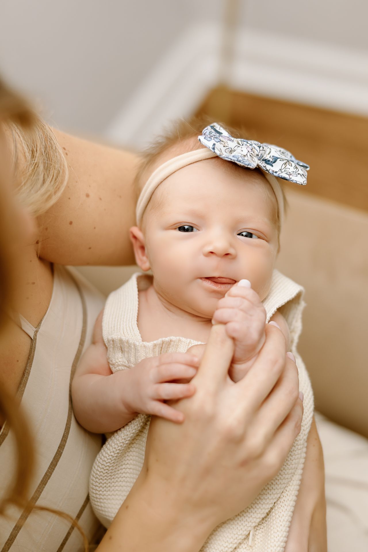 Sweet baby with bow headband smiling while being held in cream-colored setting.