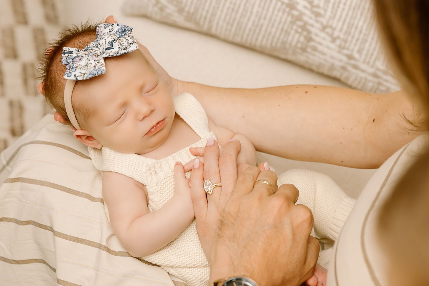 Peaceful sleeping baby with sparkly bow accessory held gently by parent's hands.