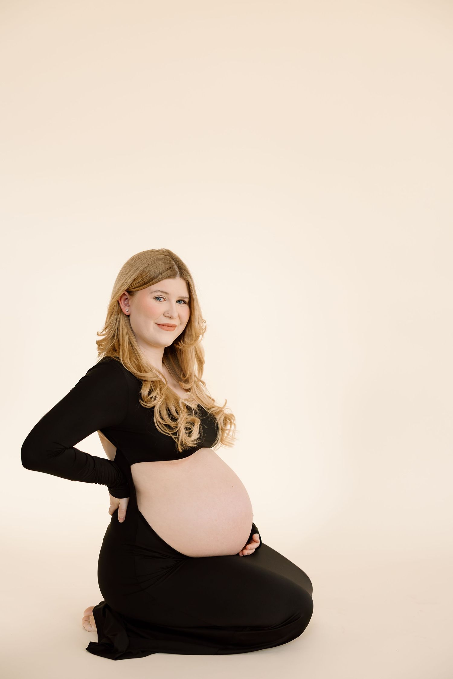Elegant maternity portrait of expectant mother wearing black dress against cream background.