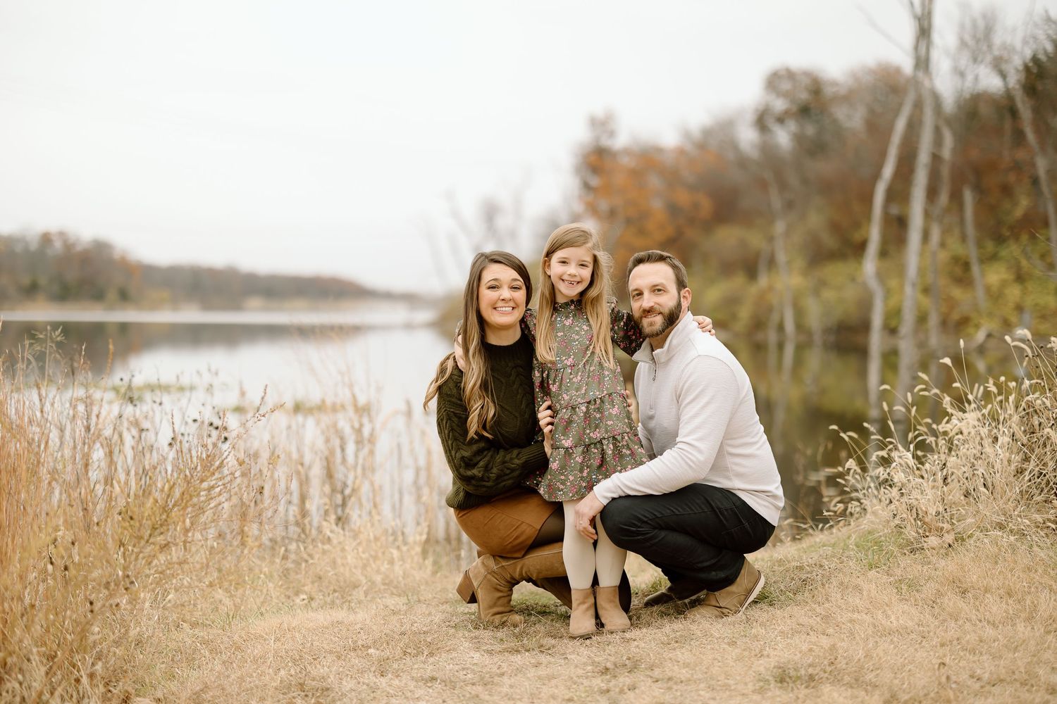 Casual family portrait by the lake with autumn colors and natural setting.
