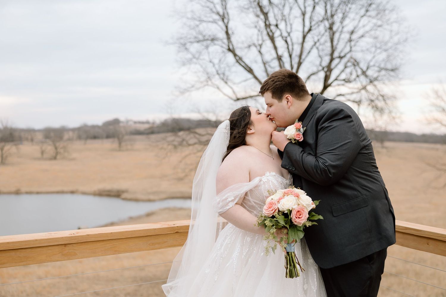 Romantic outdoor wedding portrait with couple on wooden deck overlooking water.