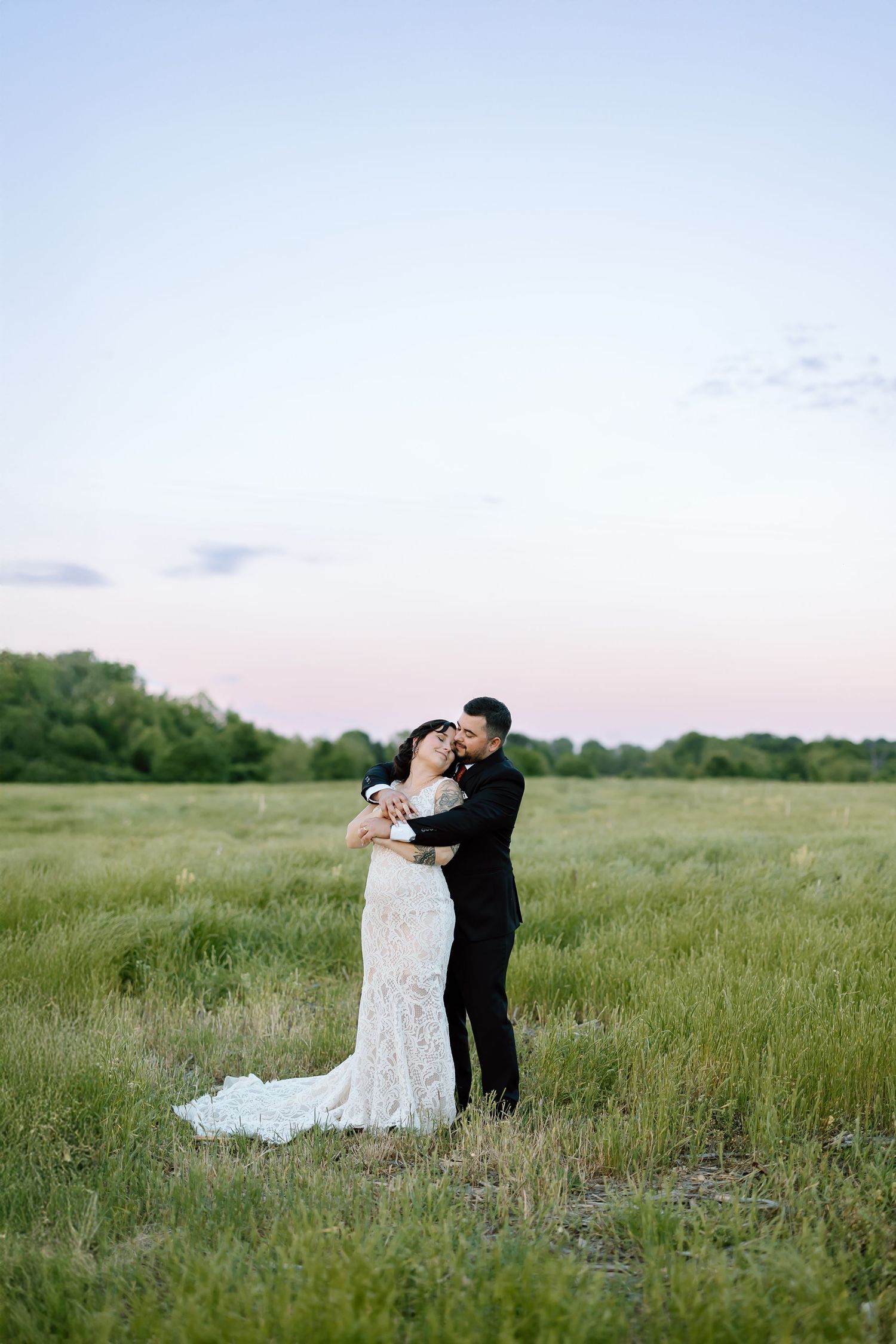 A couple shares a romantic dance together in a serene meadow of tall grass at dusk.
