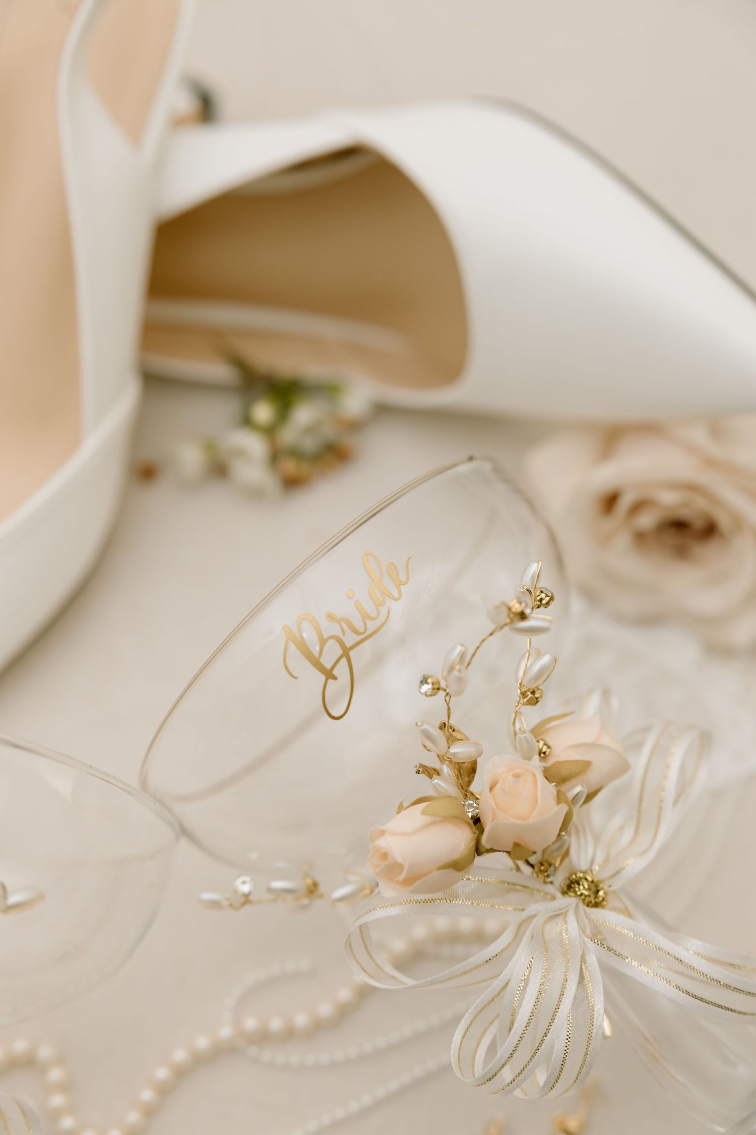 Elegant white bridal accessories including heels, delicate floral details, pearls and personalized glass with gold lettering.