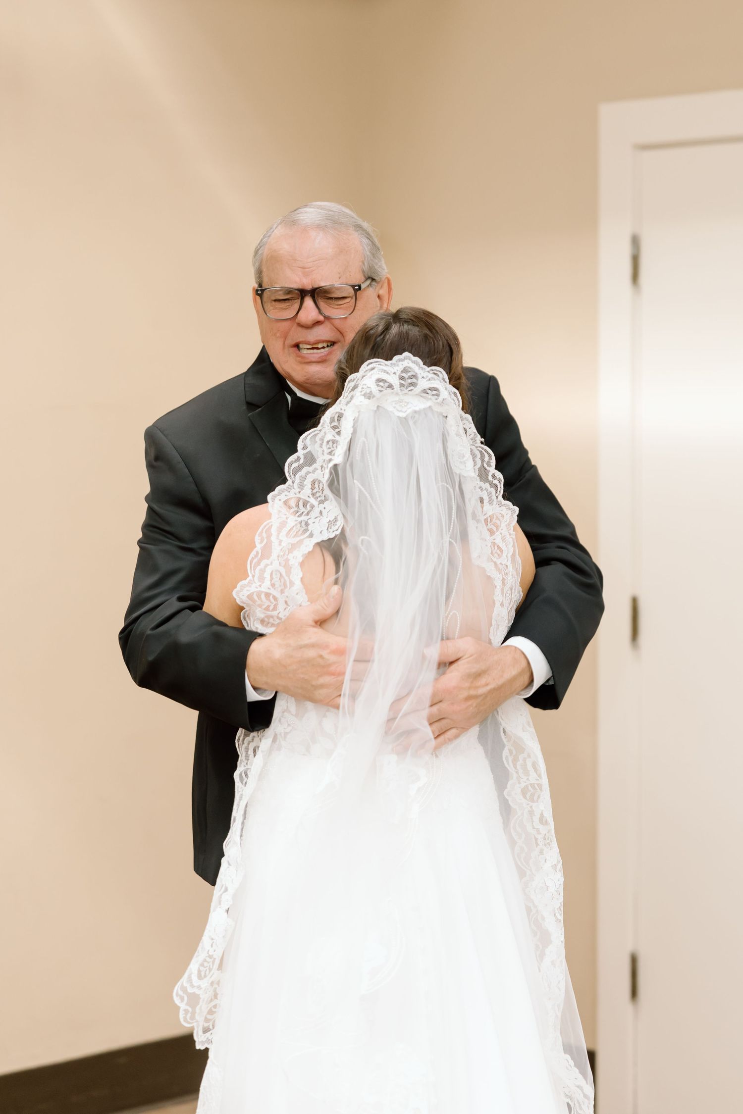 An emotional moment at a wedding as a clergy member in black suit embraces someone wearing a white lace veil.