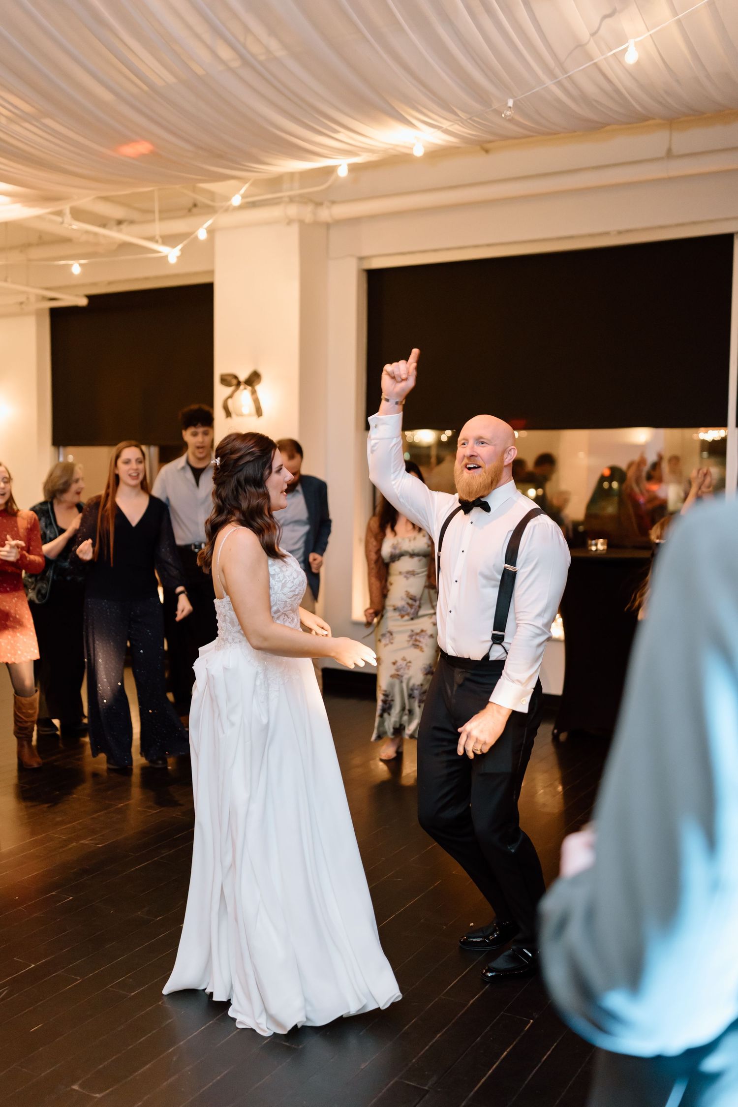 A couple dances together at a wedding reception in a venue with draped fabric ceiling and dark wood floors.