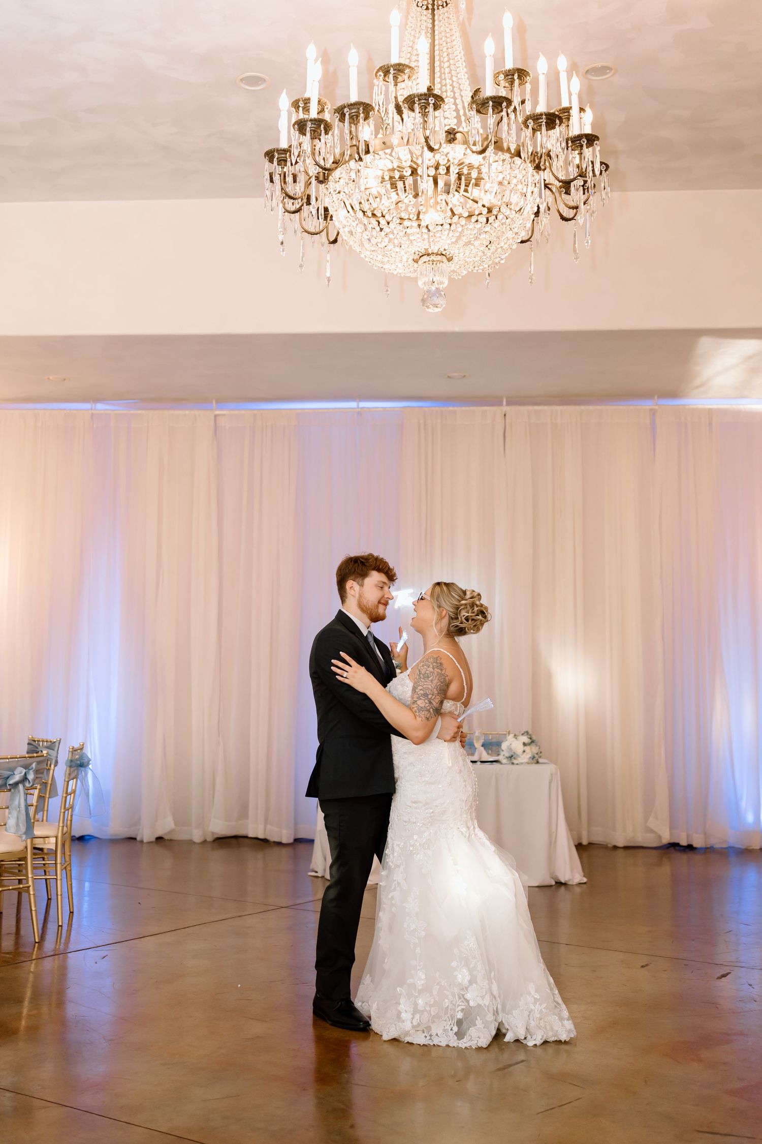 Elegant wedding ballroom with crystal chandeliers and white drapes showcasing a romantic first dance moment.