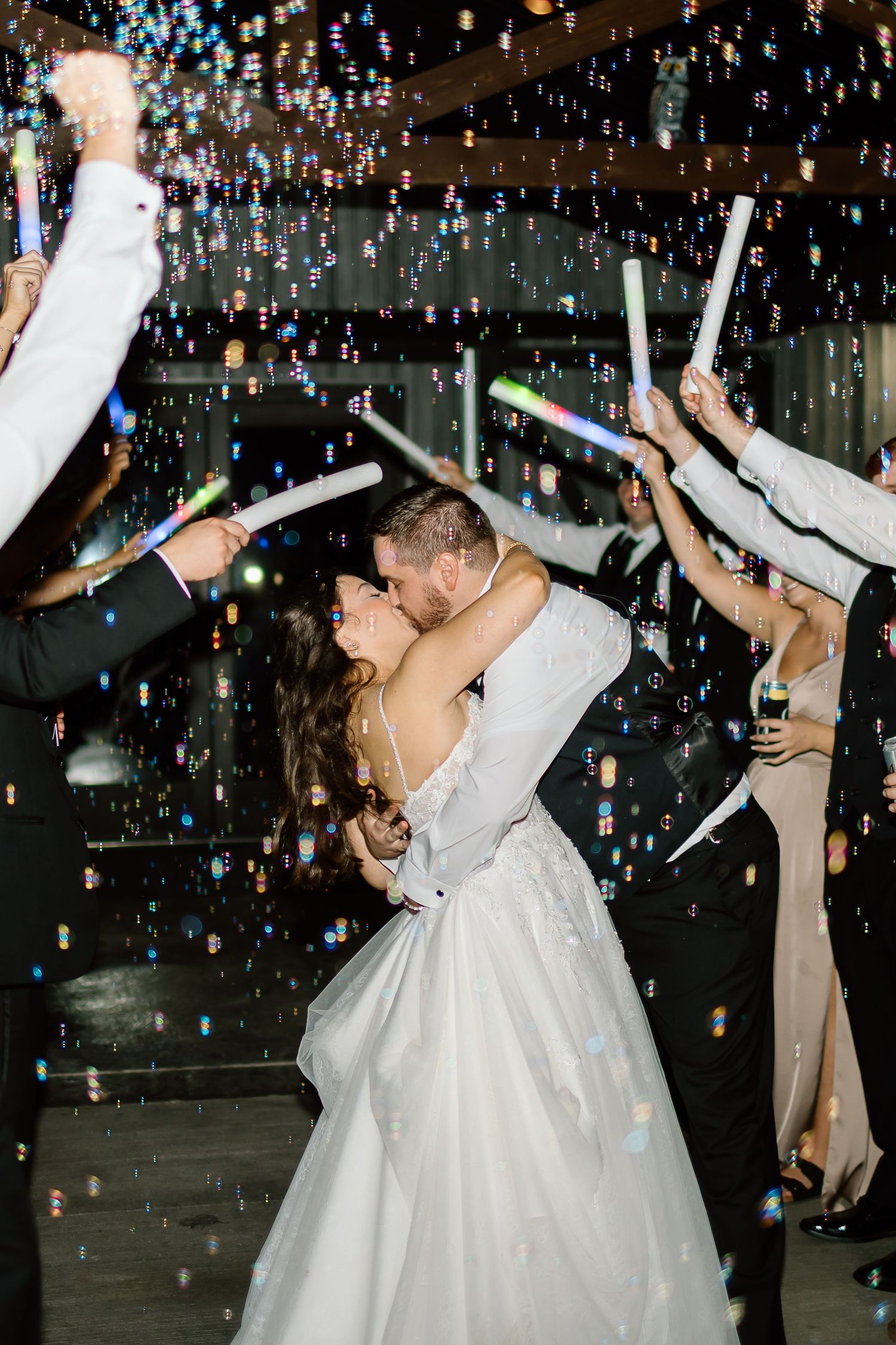 A couple shares a romantic dance under a shower of bubbles and LED foam sticks at their wedding celebration.