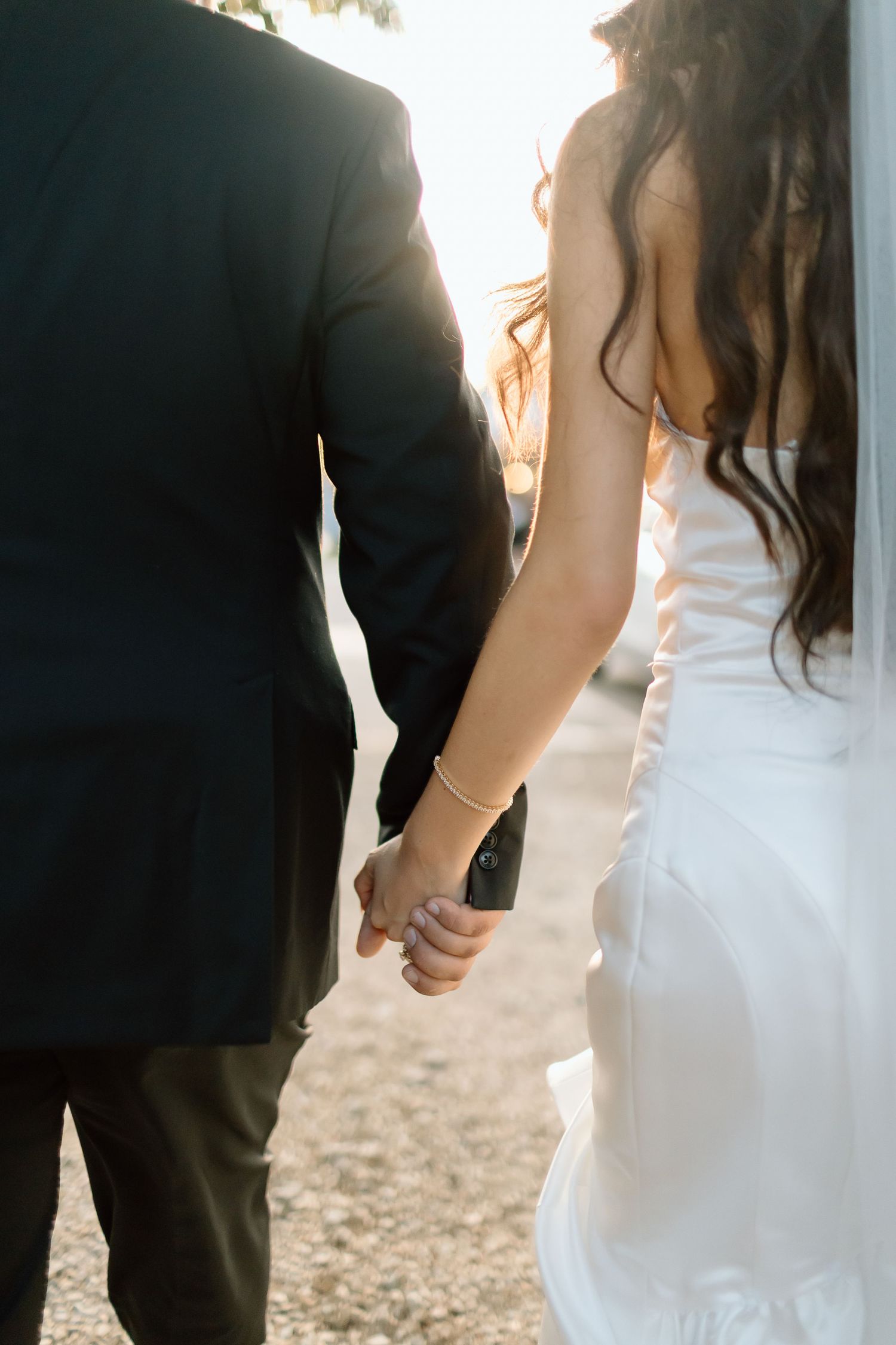 Cropped view of newlywed couple holding hands while walking together outdoors at sunset.