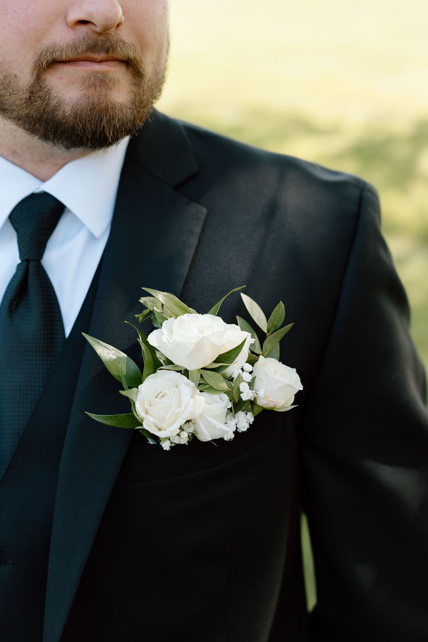 White floral boutonnieres pinned to black suit lapels create an elegant formal look at a wedding ceremony.