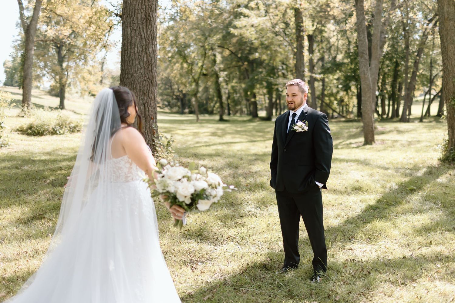 A romantic wedding couple walks together through a sunlit forest with tall trees creating a natural outdoor setting.