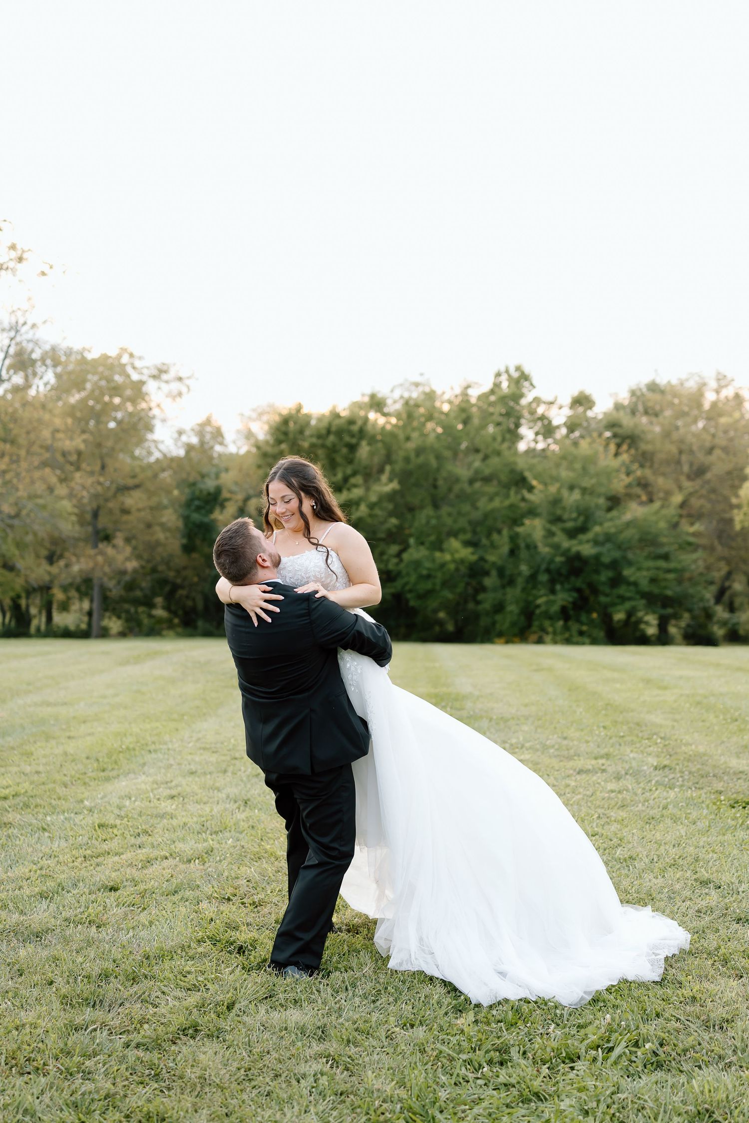 A romantic dance unfolds between a couple in wedding attire on a scenic grassy field.