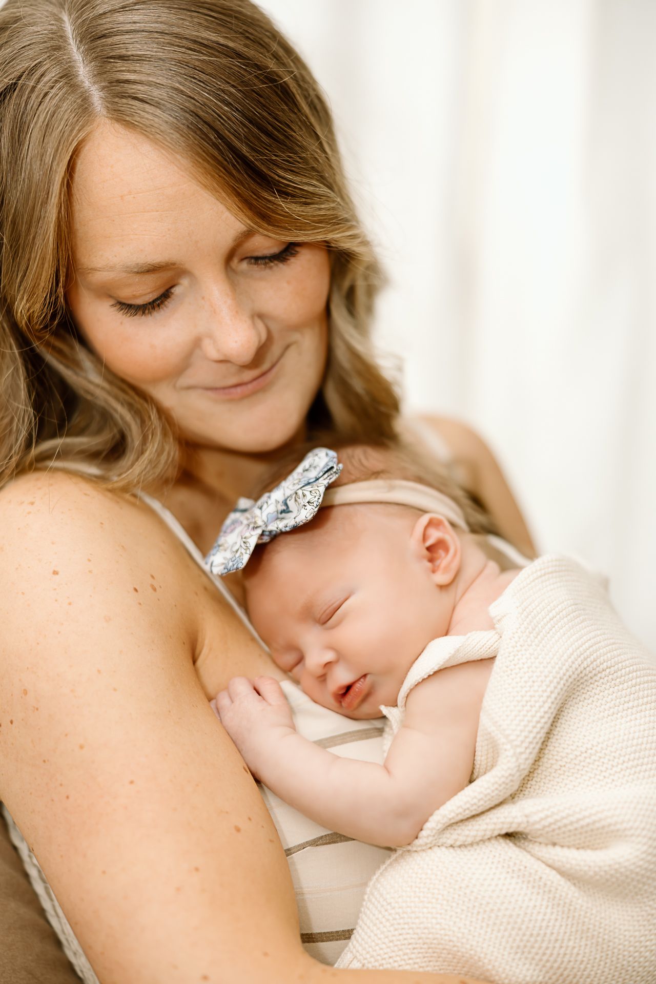 Tender moment of a sleeping newborn wearing a decorative bow headband resting against soft fabric.