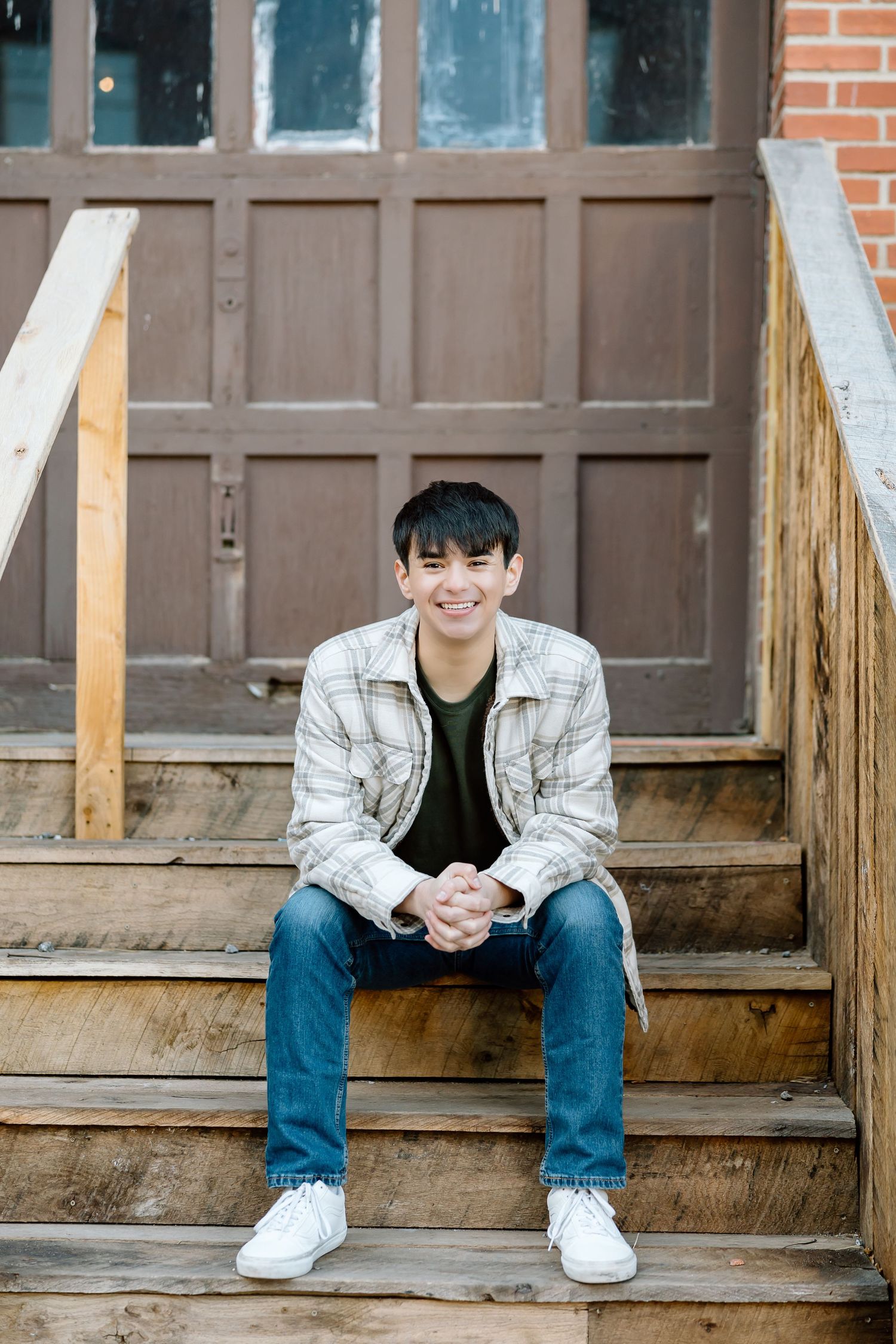 Person in light plaid jacket sitting relaxed on wooden stairs.