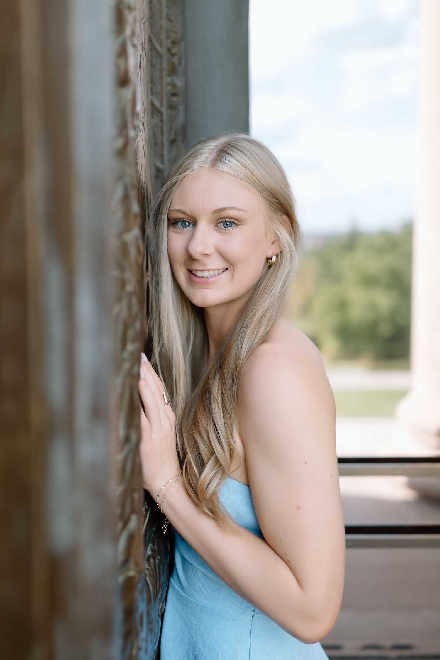 A person in a light blue sleeveless top poses against a window in a series of connected portrait shots.