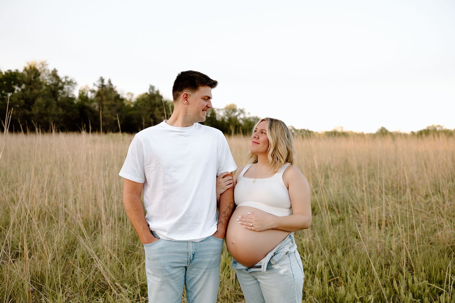 Couple in casual attire sharing intimate moments in a golden wheat field during sunset.