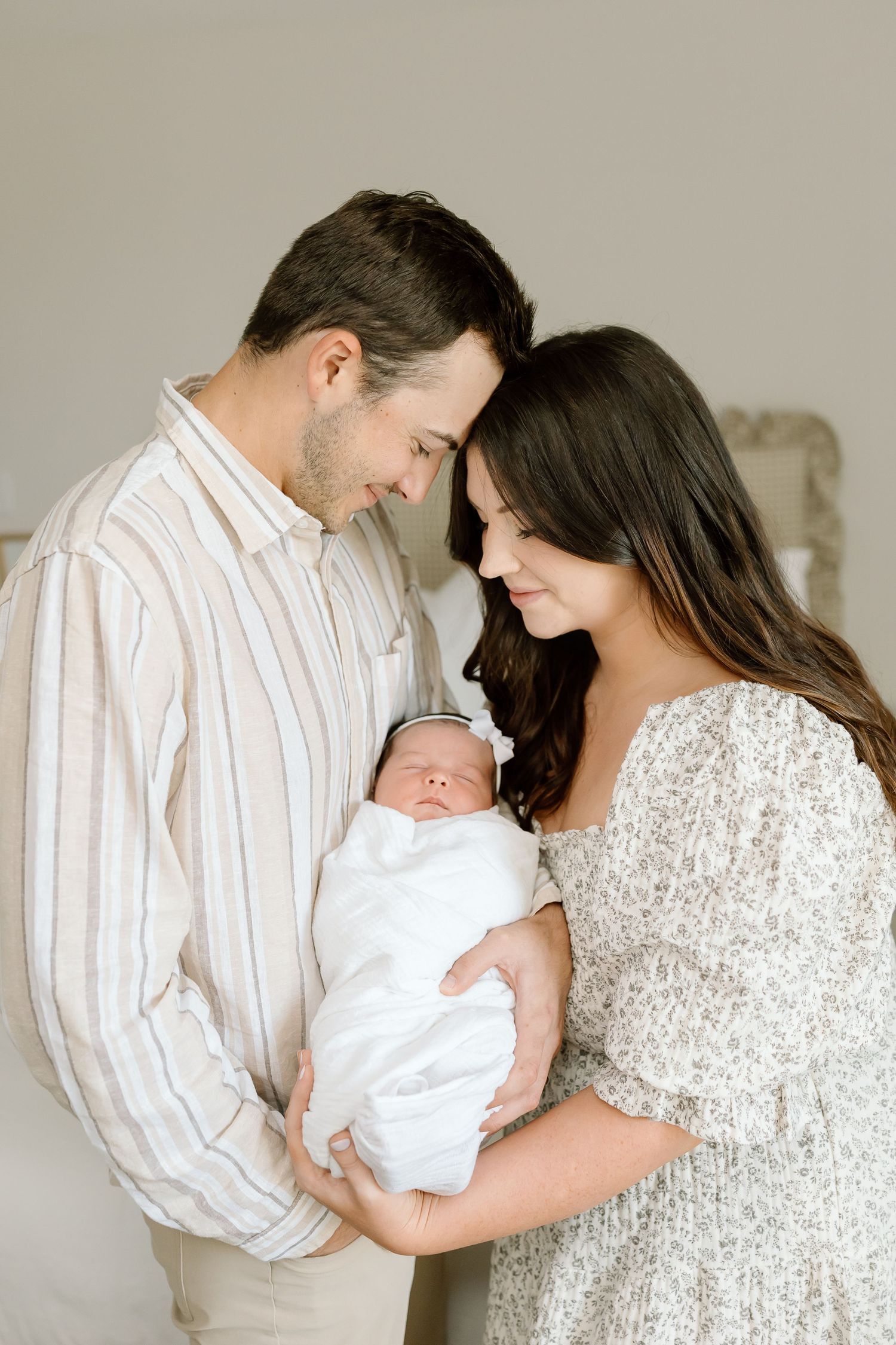 A couple in white and beige clothing holds their newborn baby in a series of tender family portrait poses.